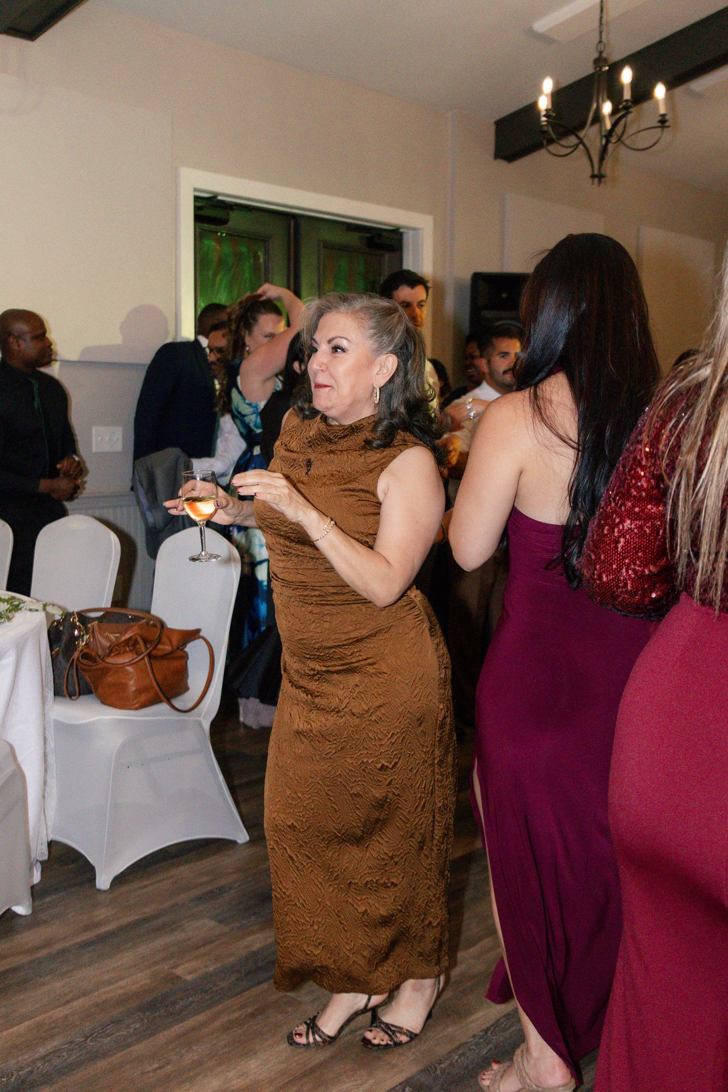 A group of people in formal attire dancing at an indoor event with white chair covers and wood flooring. Aiken Wedding Photographer