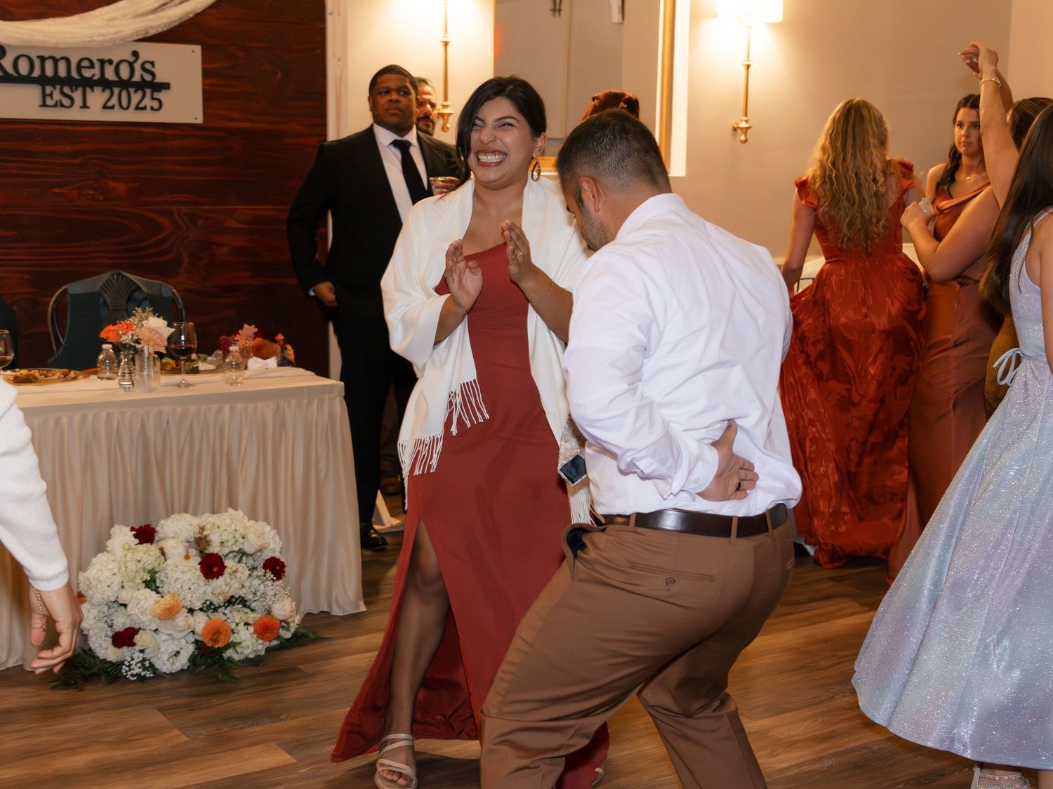 Wedding guests dance together on a wooden floor during a reception celebration with warm lighting and decor. Lexington Wedding Photographer