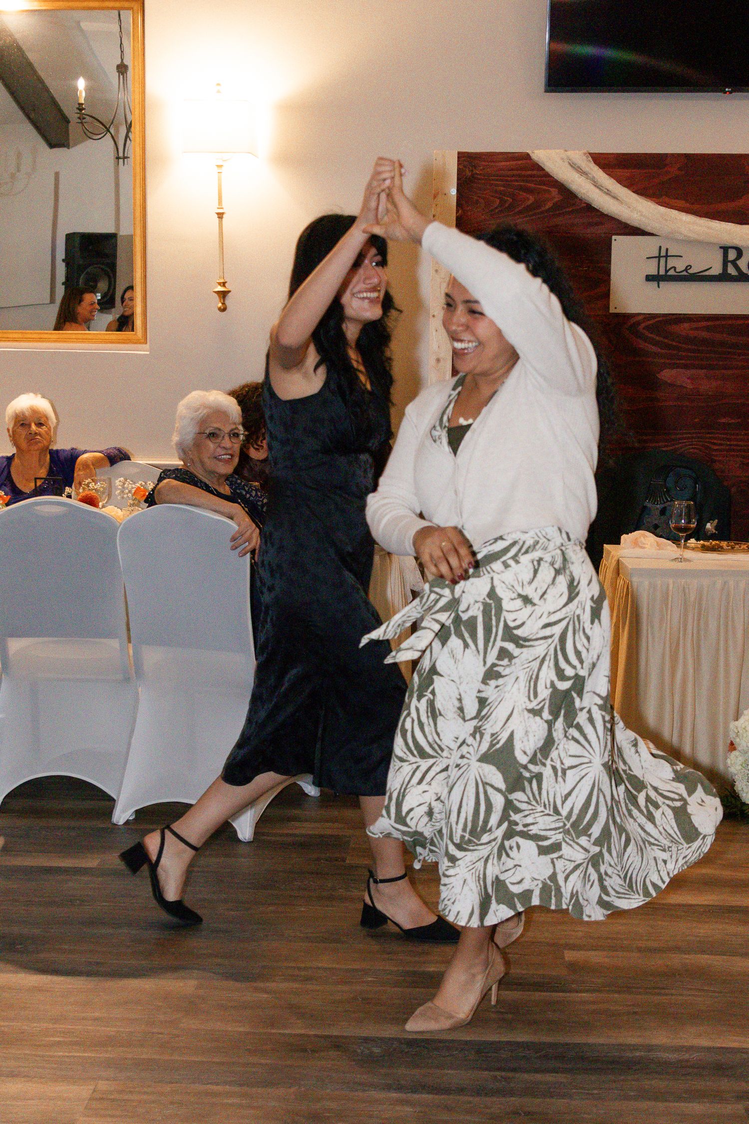 Two women in contrasting black and white outfits dance together joyfully on a wooden dance floor at an indoor event. Lexington Wedding Photo