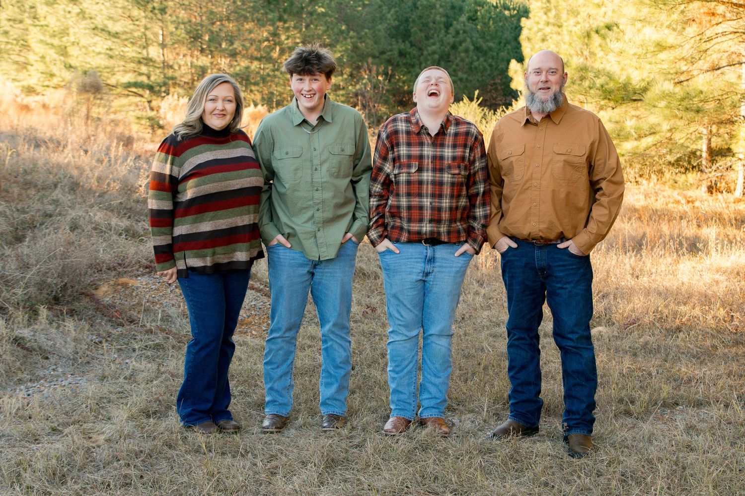 A family of four laughs joyfully together in an open field during golden autumn light.
