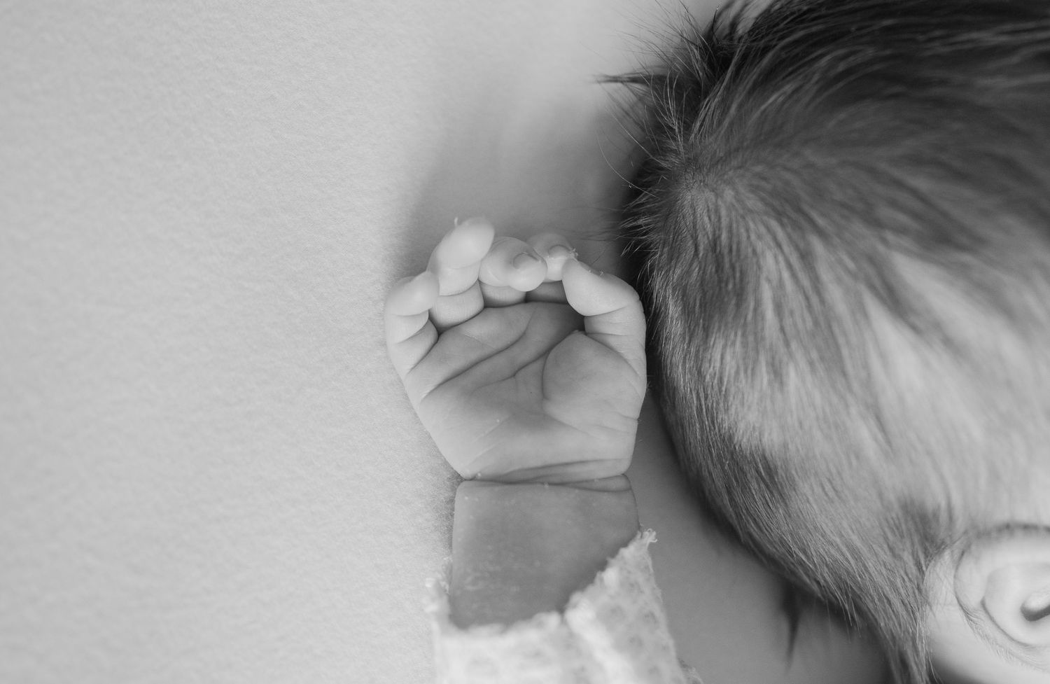Black and white photo of a sleeping newborn baby with tiny clenched fist resting beside their head.