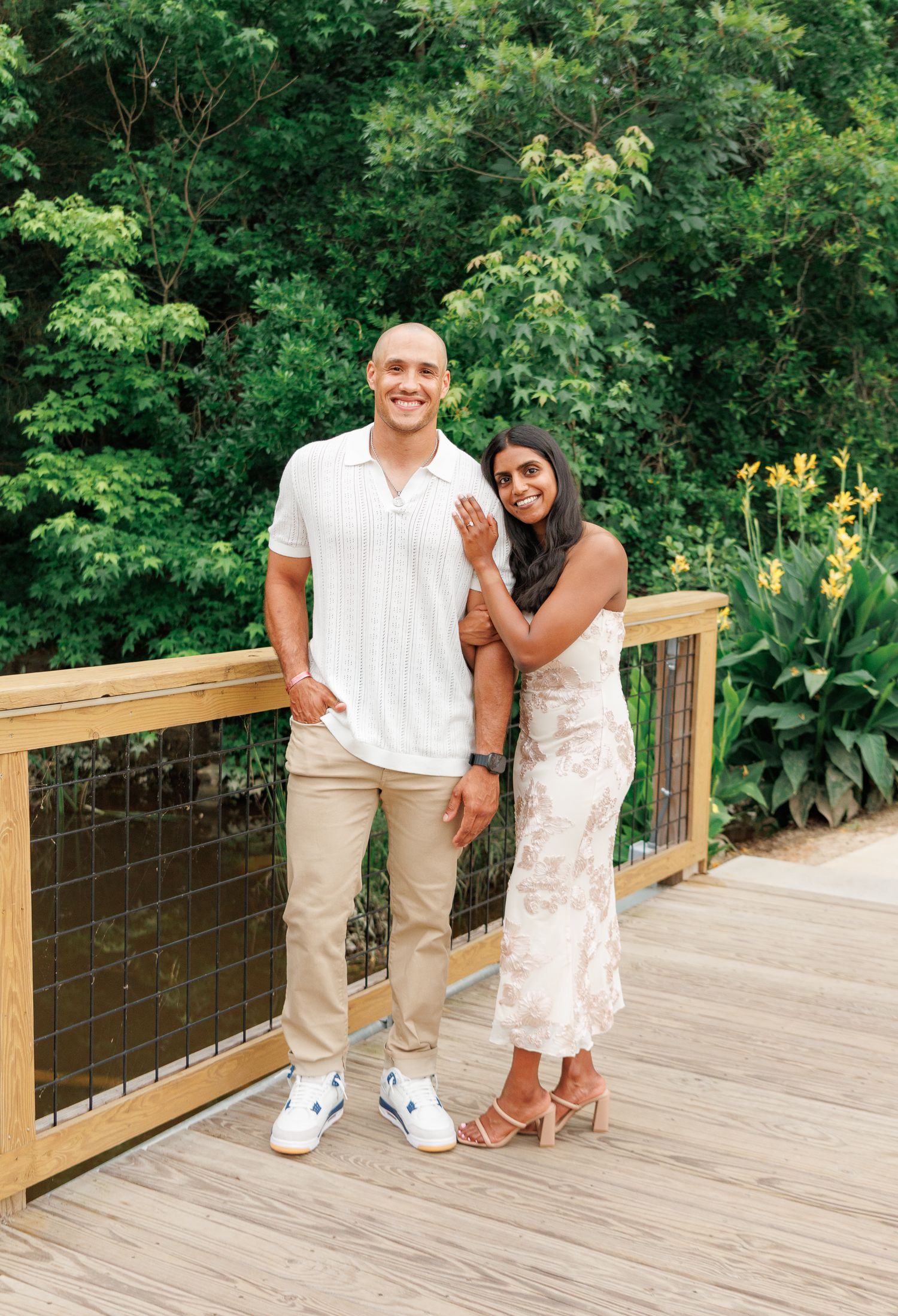Smiling couple posing together on a wooden deck surrounded by vibrant green foliage.