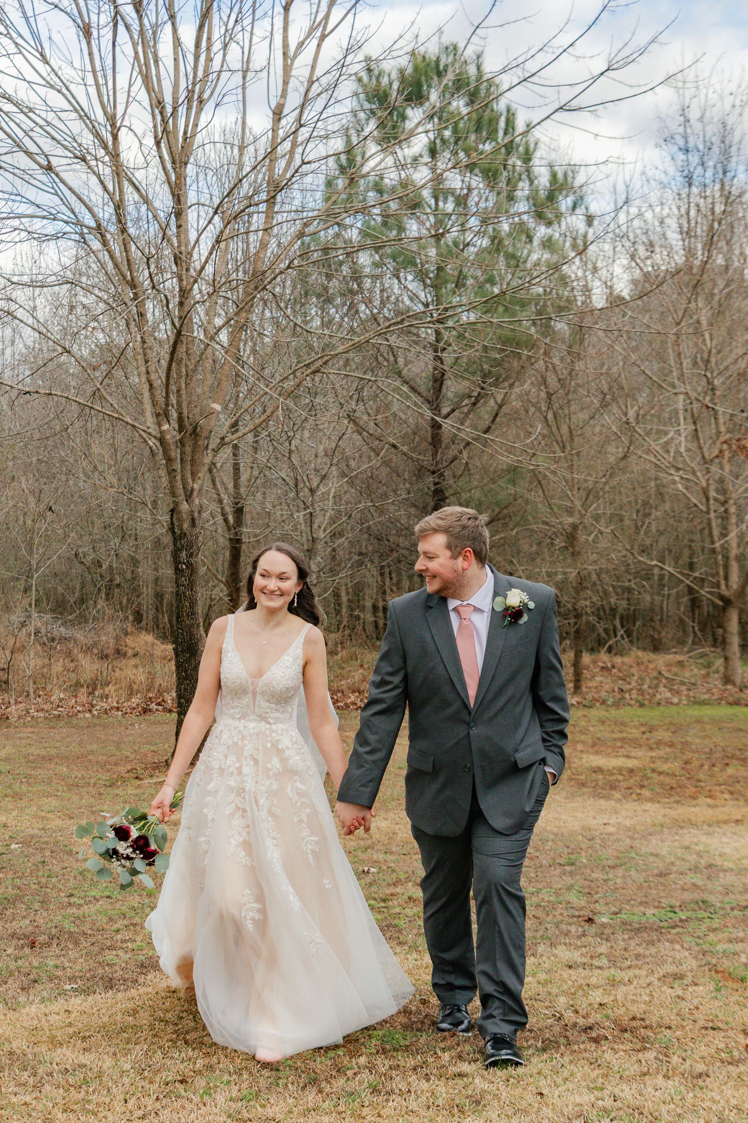 A couple walks together in a wooded outdoor setting during their wedding photoshoot.