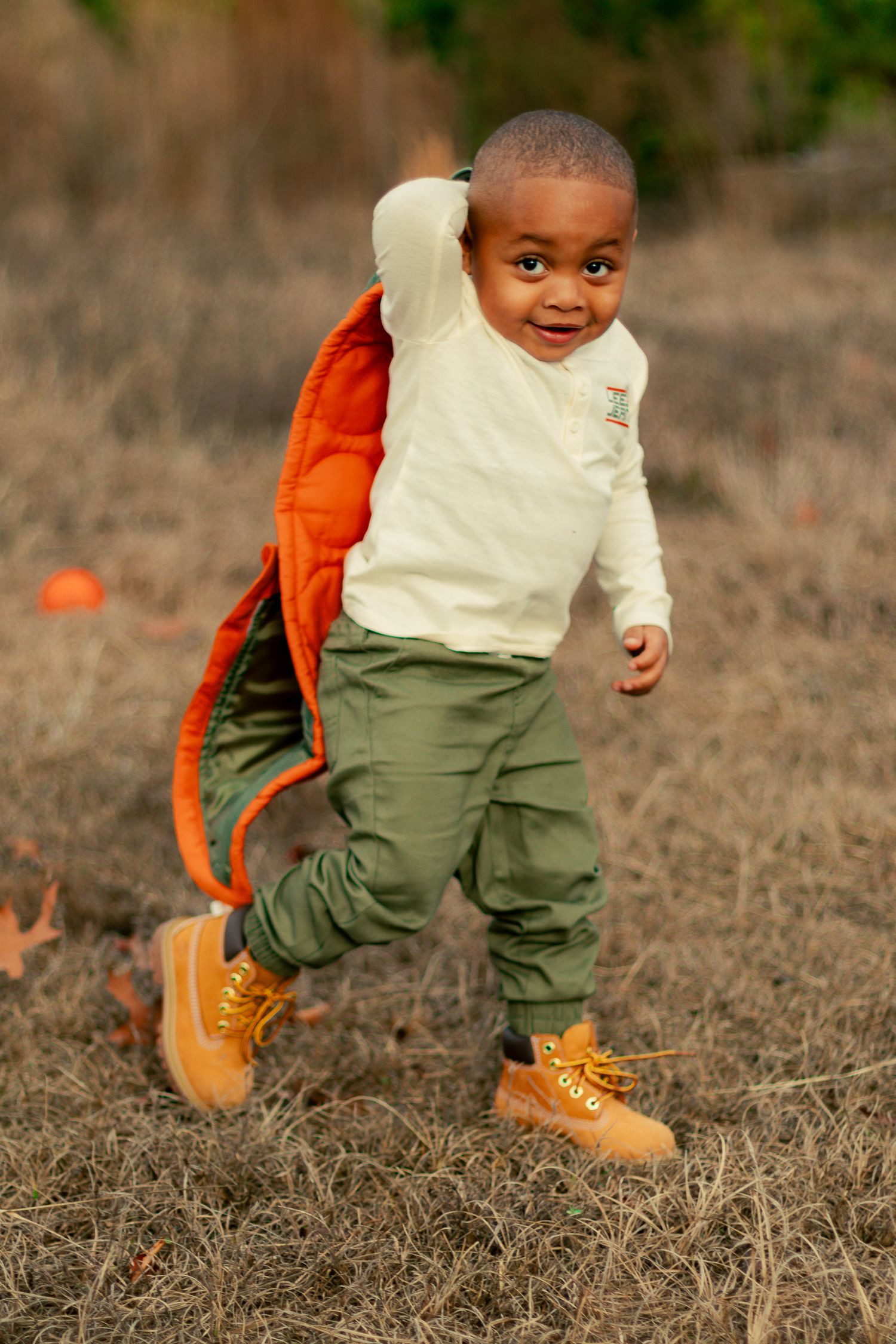 A child in a white shirt, olive pants and orange boots walks across dry grass in a sequence of motion shots.