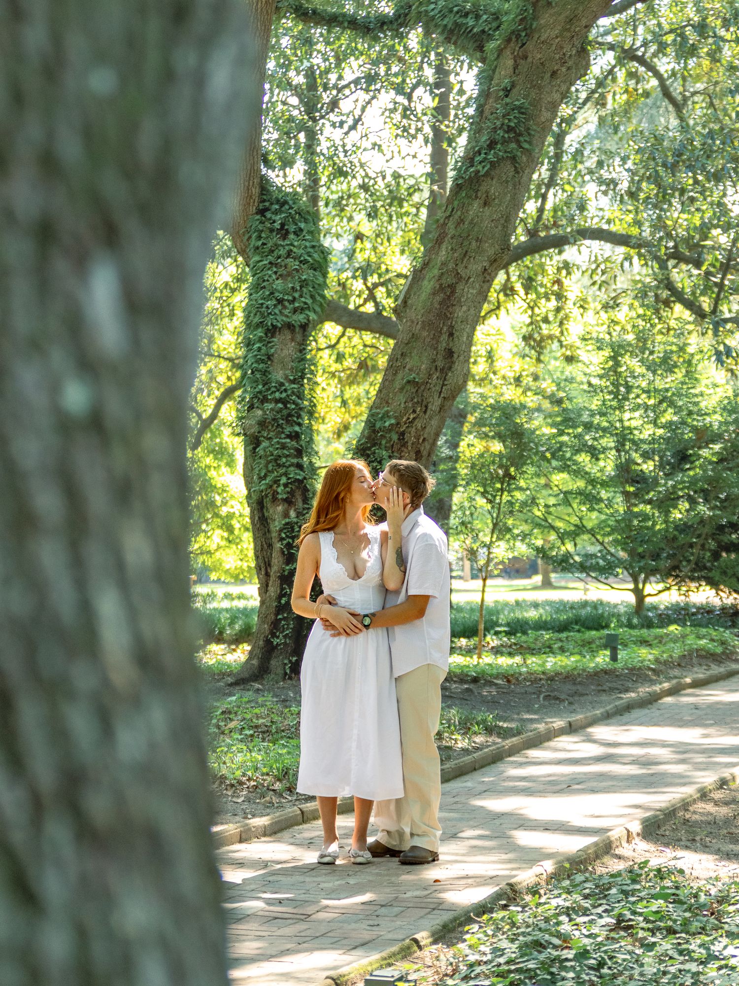 Engaged couple sharing a kiss on a sunlit garden path during an Aiken, South Carolina engagement session.