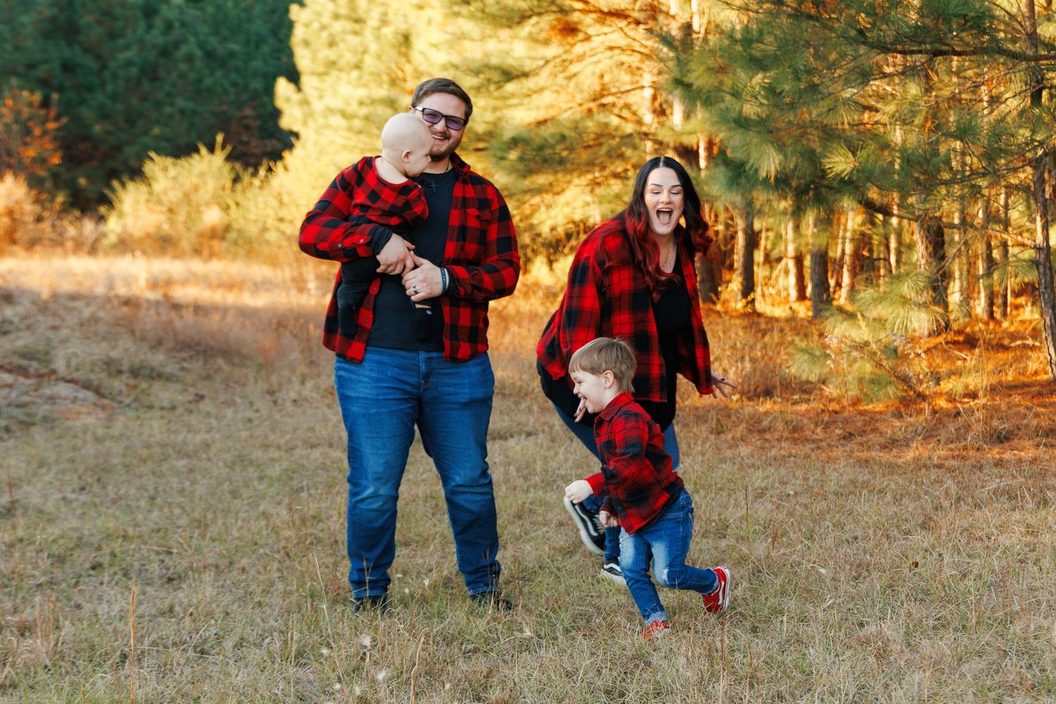 A family in matching red plaid outfits plays and laughs together in a sunny autumn field.