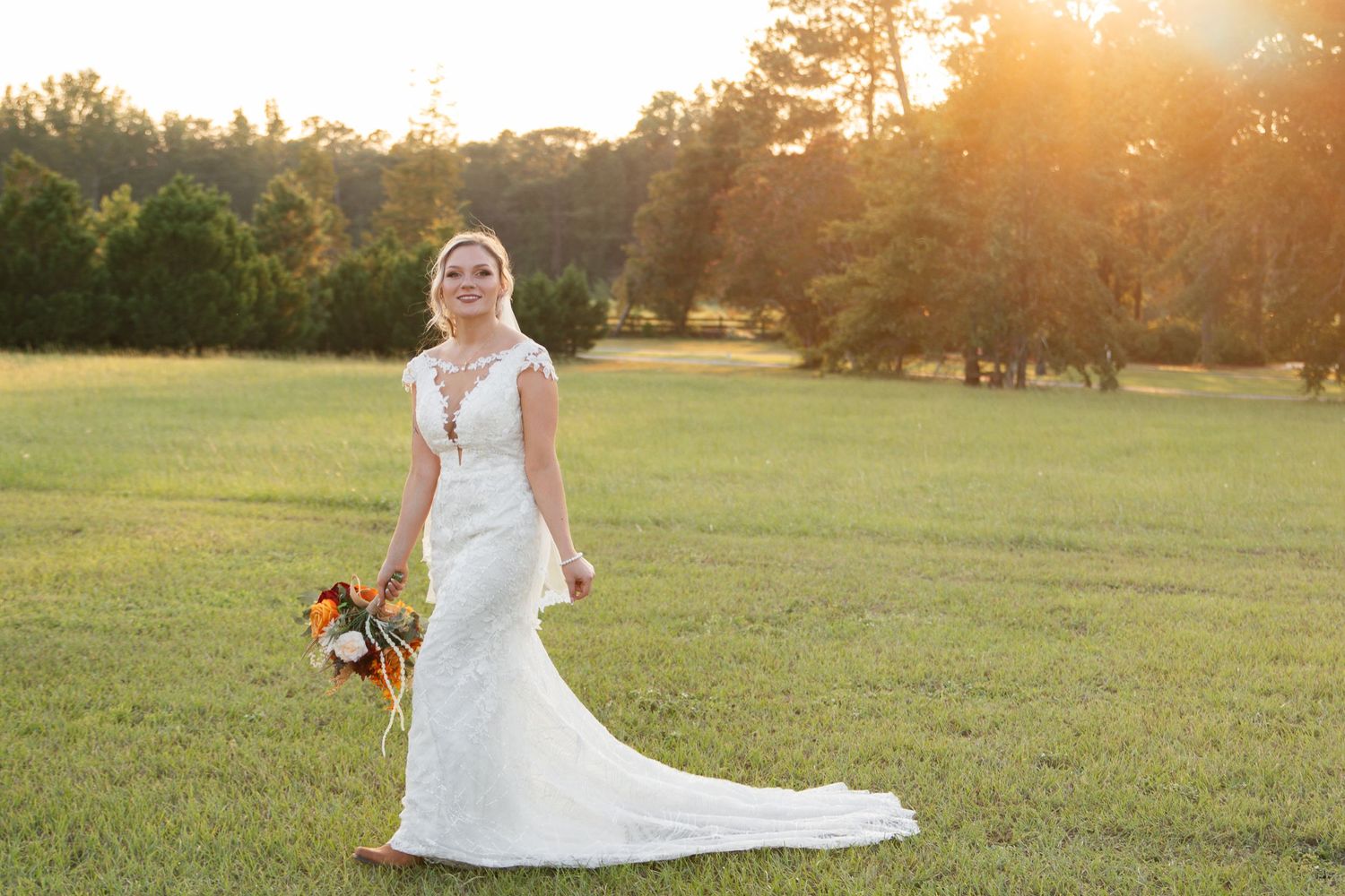 A wedding couple embraces in a golden-lit field during sunset, creating a romantic silhouette against the warm sky.