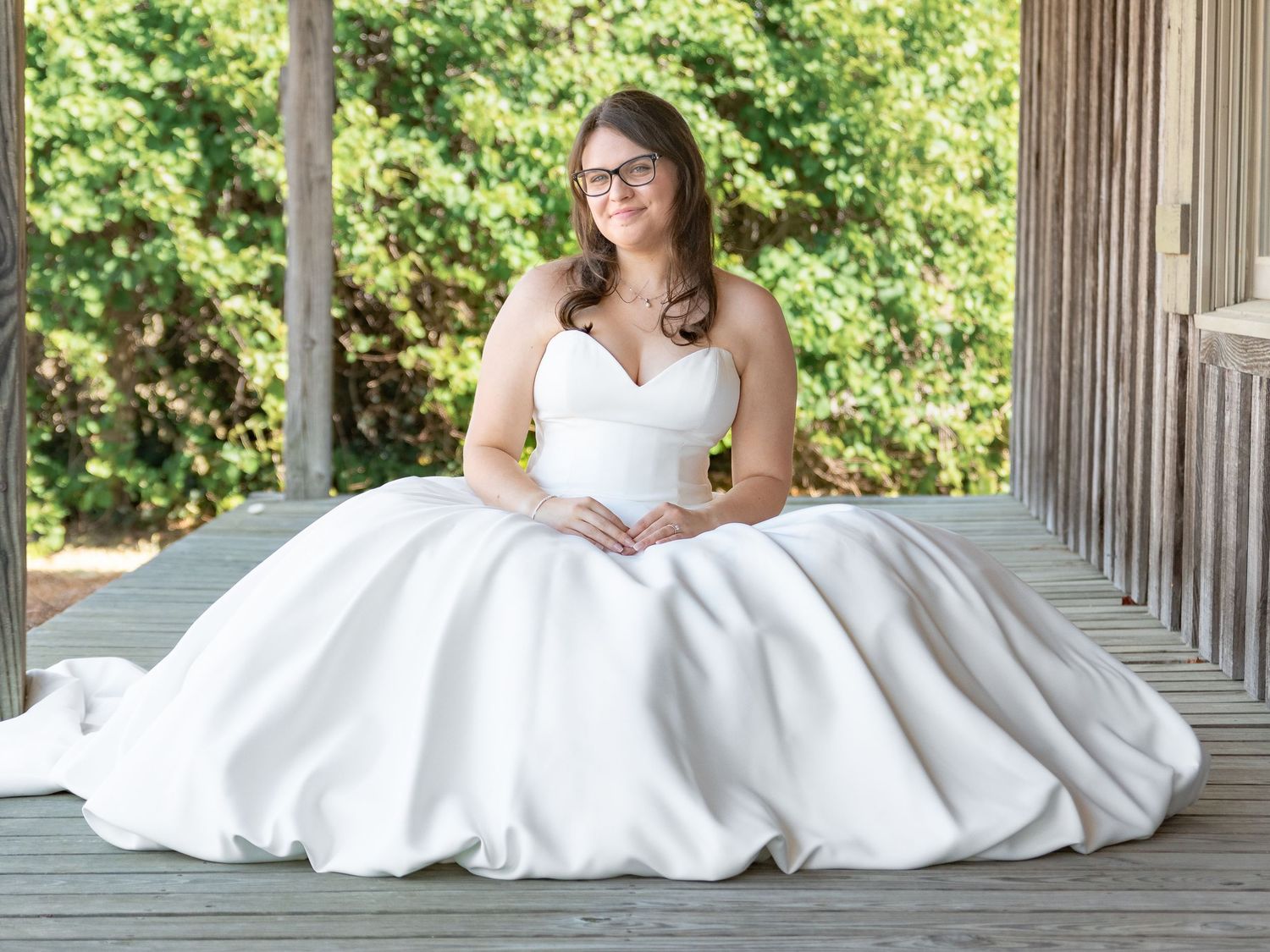 Bride in a strapless white ball gown sitting on a wooden deck during a South Carolina bridal portrait session.