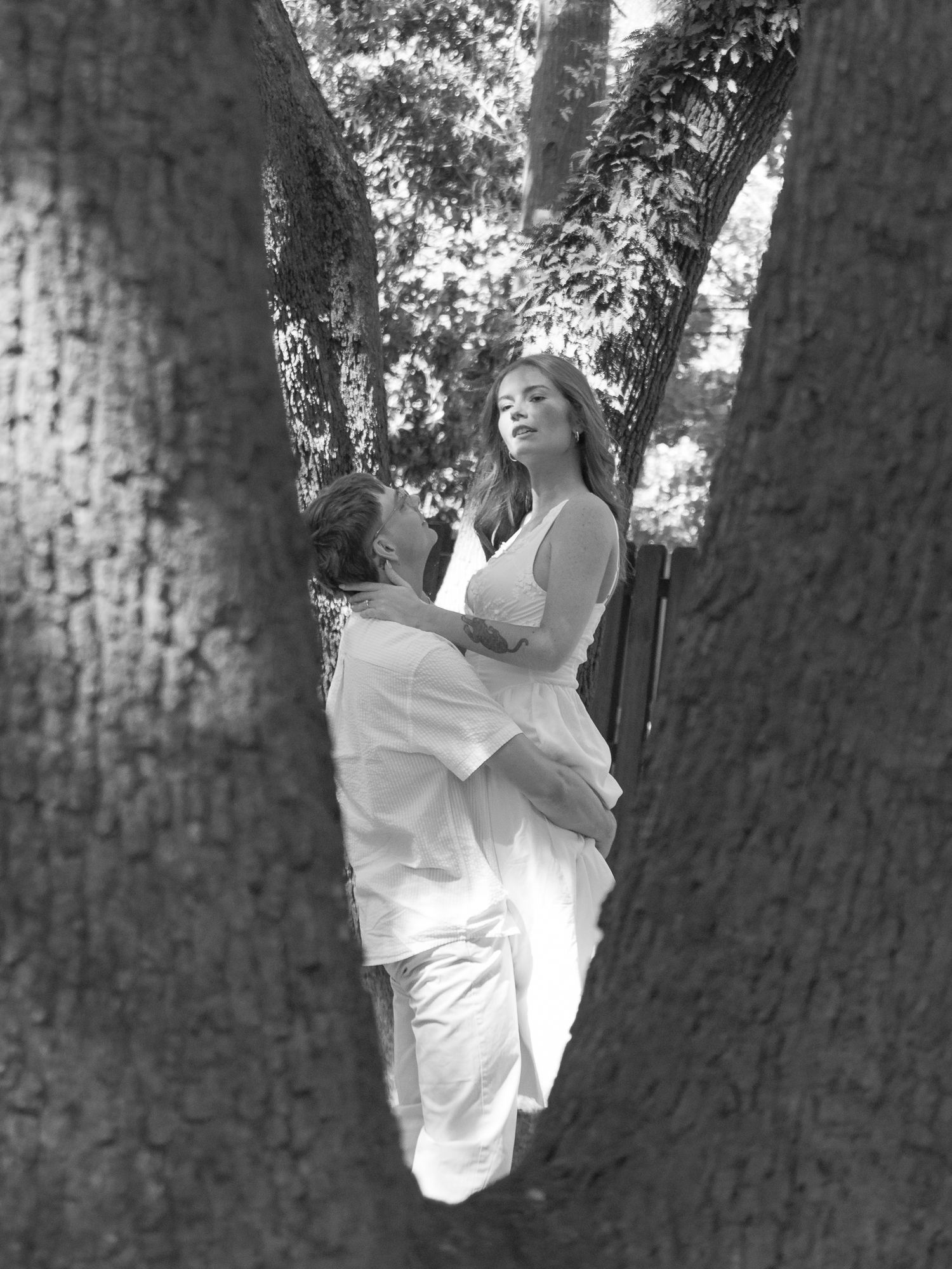 Black and white engagement portrait of a couple embracing between large oak trees in Aiken, South Carolina.
