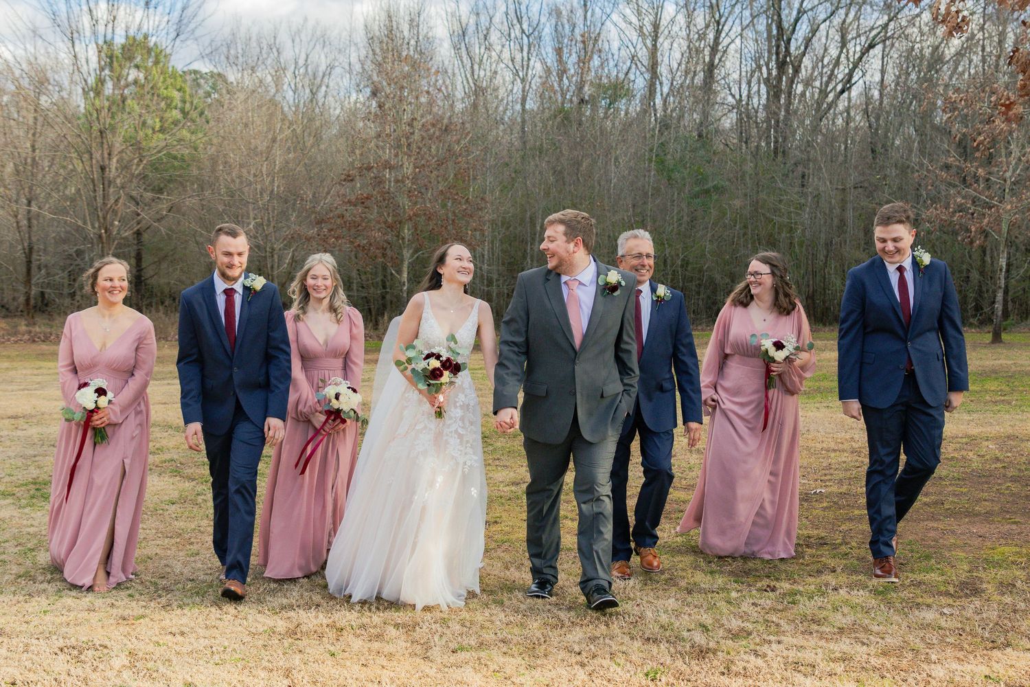 Wedding party in dusty rose and navy attire walks together outdoors during a winter photo session.
