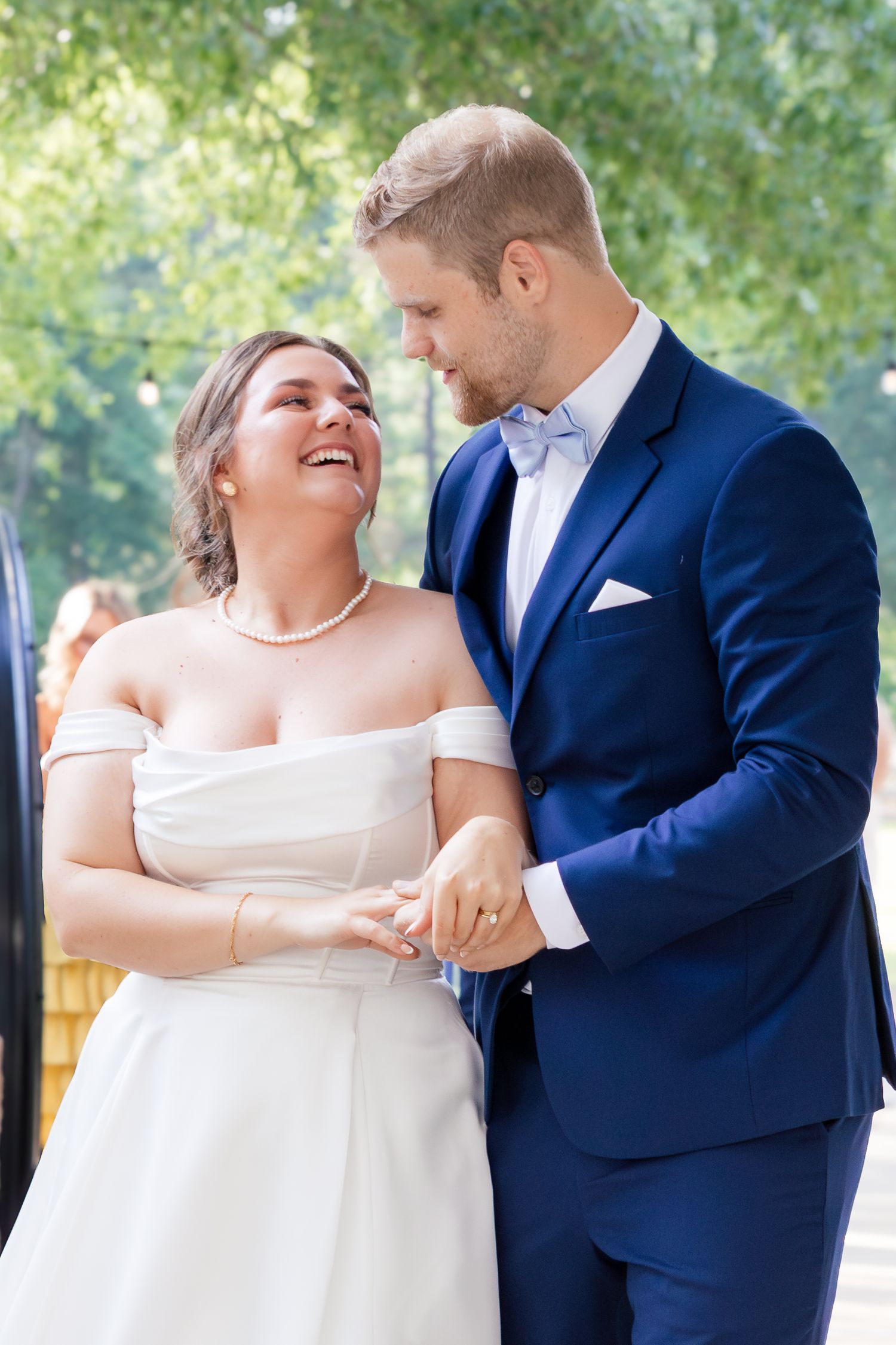 A joyful couple in wedding attire share a candid moment outdoors, the bride in white and groom in navy blue.