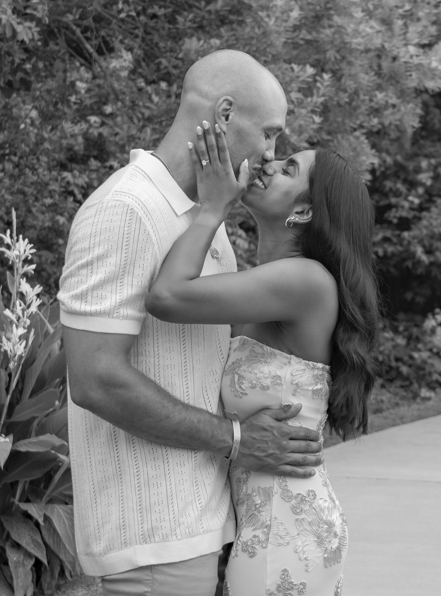 Black and white photo of a couple sharing a romantic kiss outdoors.