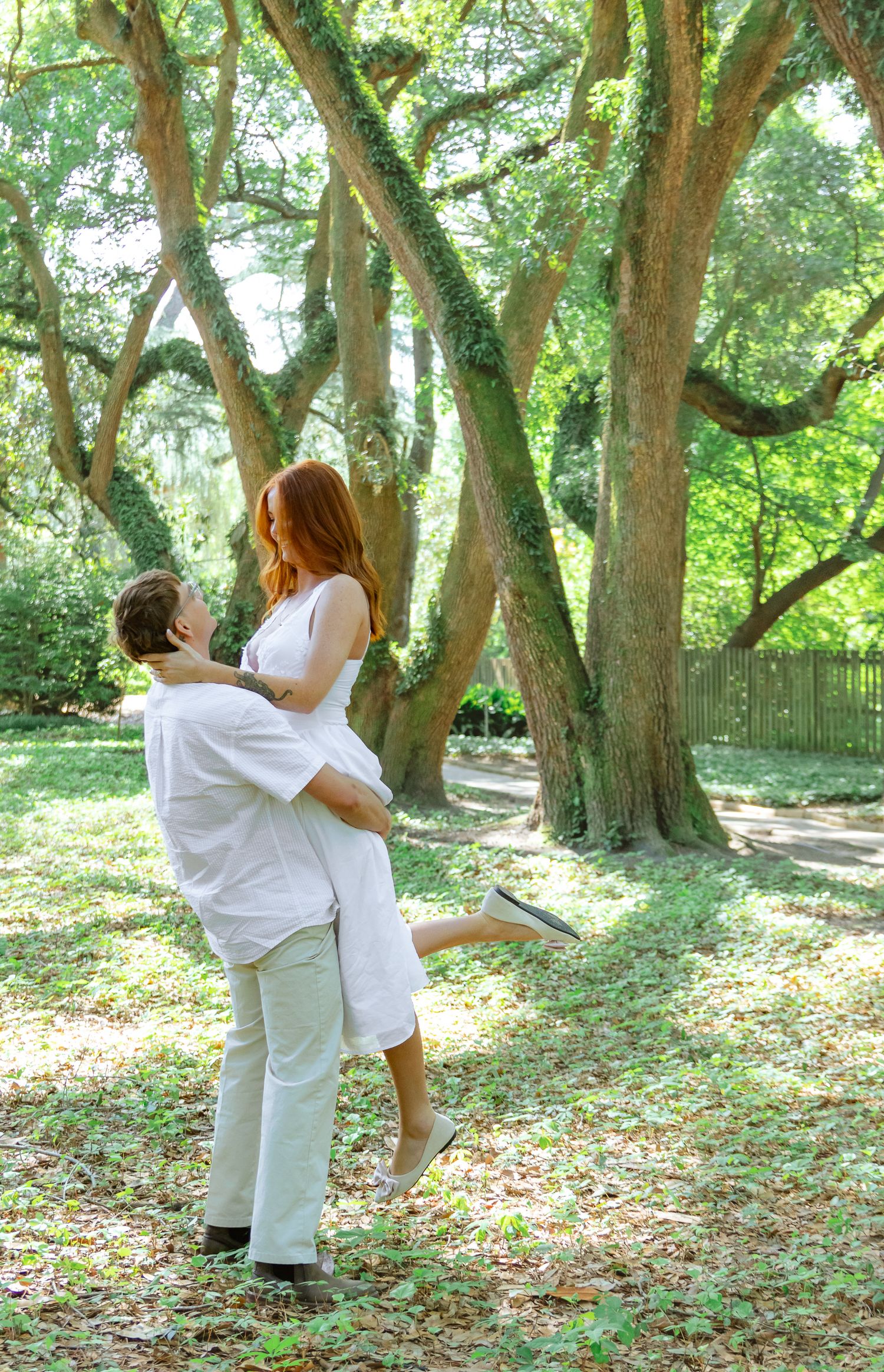 Engaged couple embracing as the groom lifts his partner among moss-covered trees during an Aiken, South Carolina engagement session.