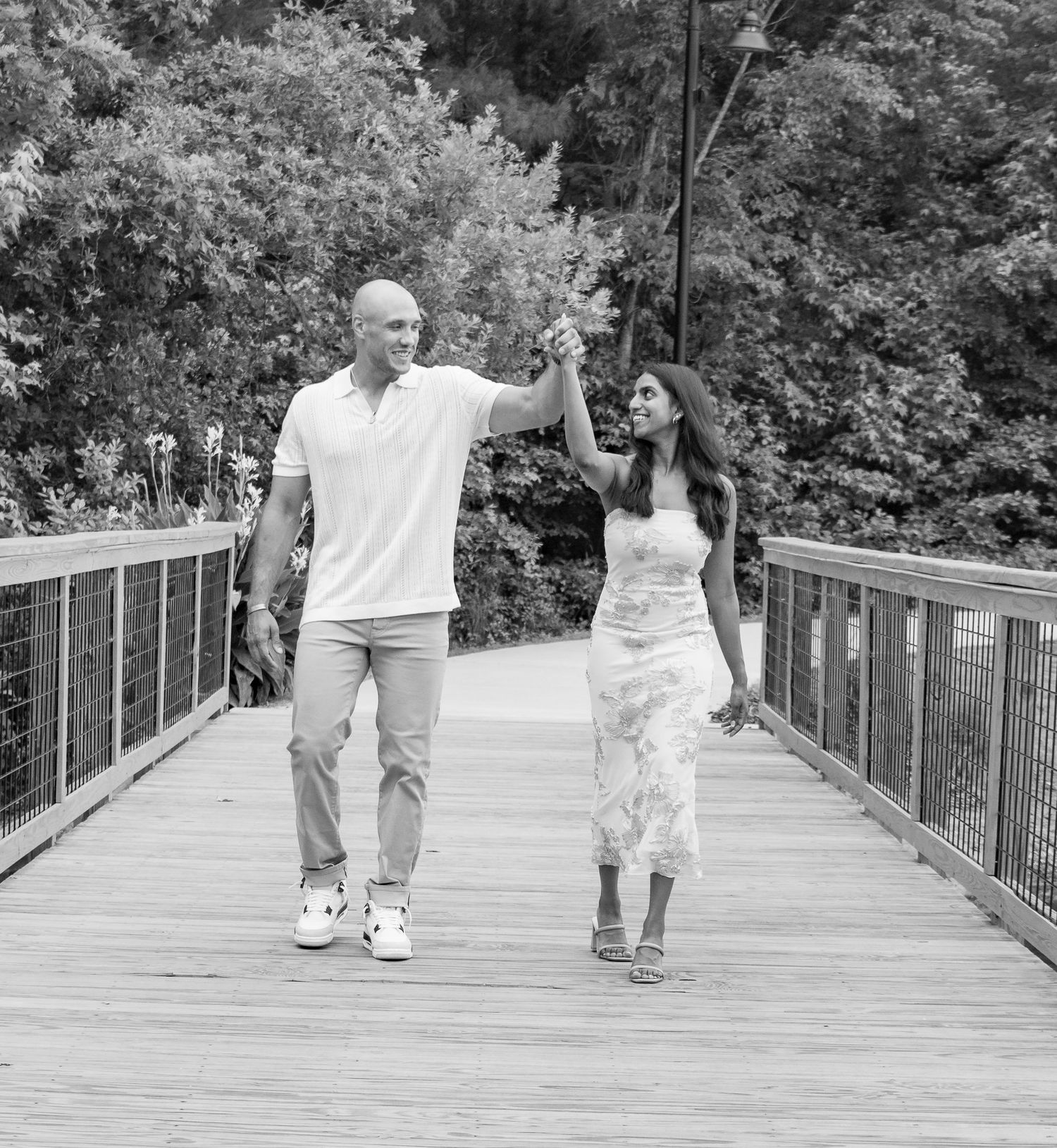 Black and white photo of a couple holding hands while walking on a wooden bridge.