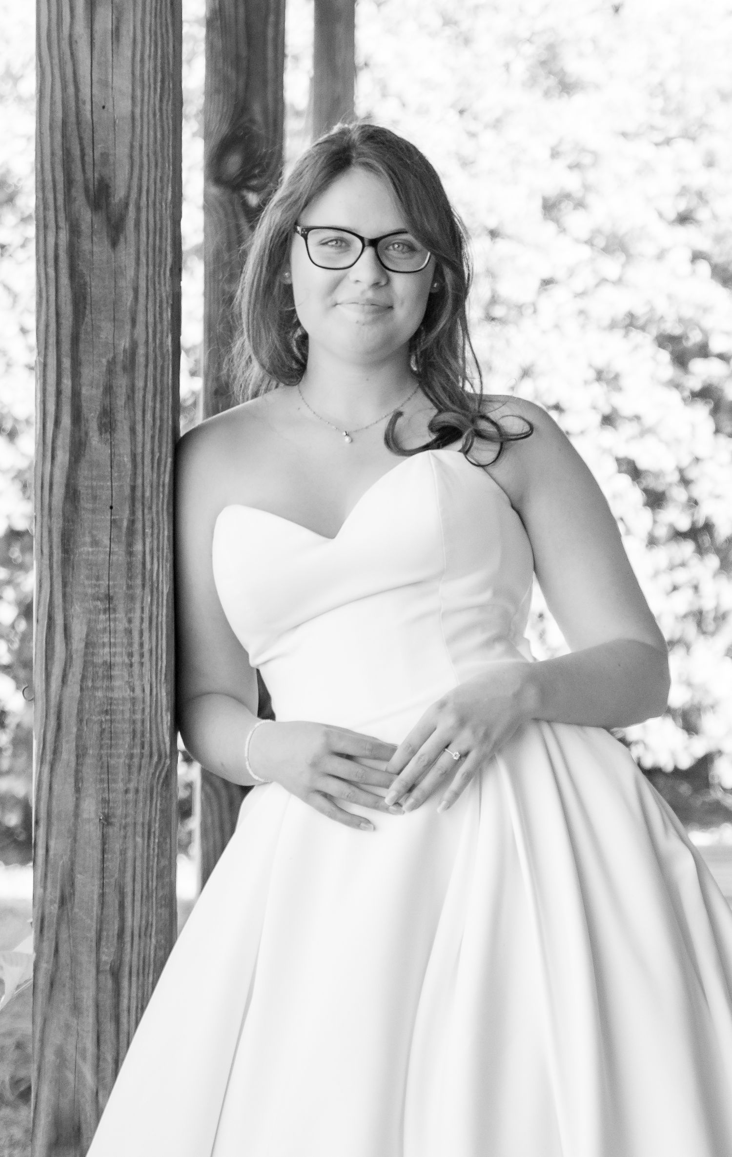 Black and white bridal portrait of a bride in a strapless white ball gown and glasses.