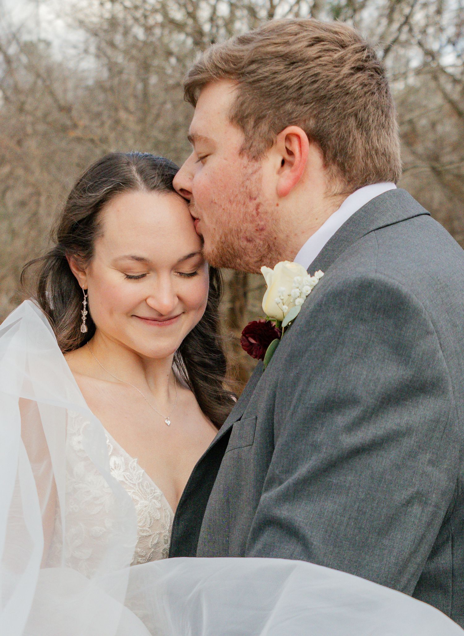 A romantic moment captured between a couple in formal wedding attire against a natural outdoor backdrop.