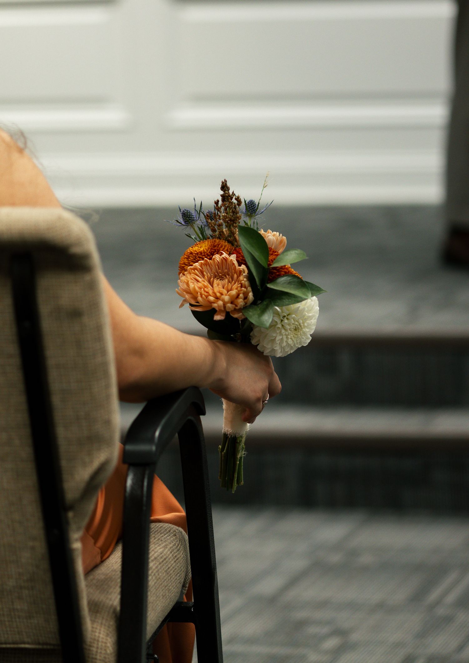 A hand holding a small orange and white floral corsage or boutonniere against a blurred background. South Carolina Wedding Photographer
