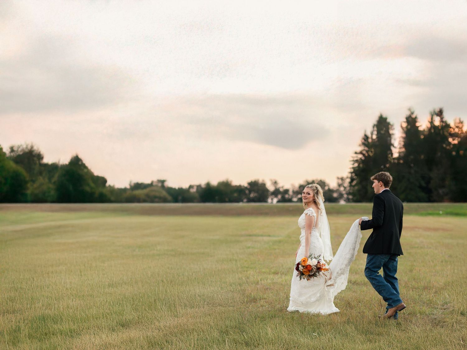 Bride and groom walking through a green field at sunset during their outdoor wedding.