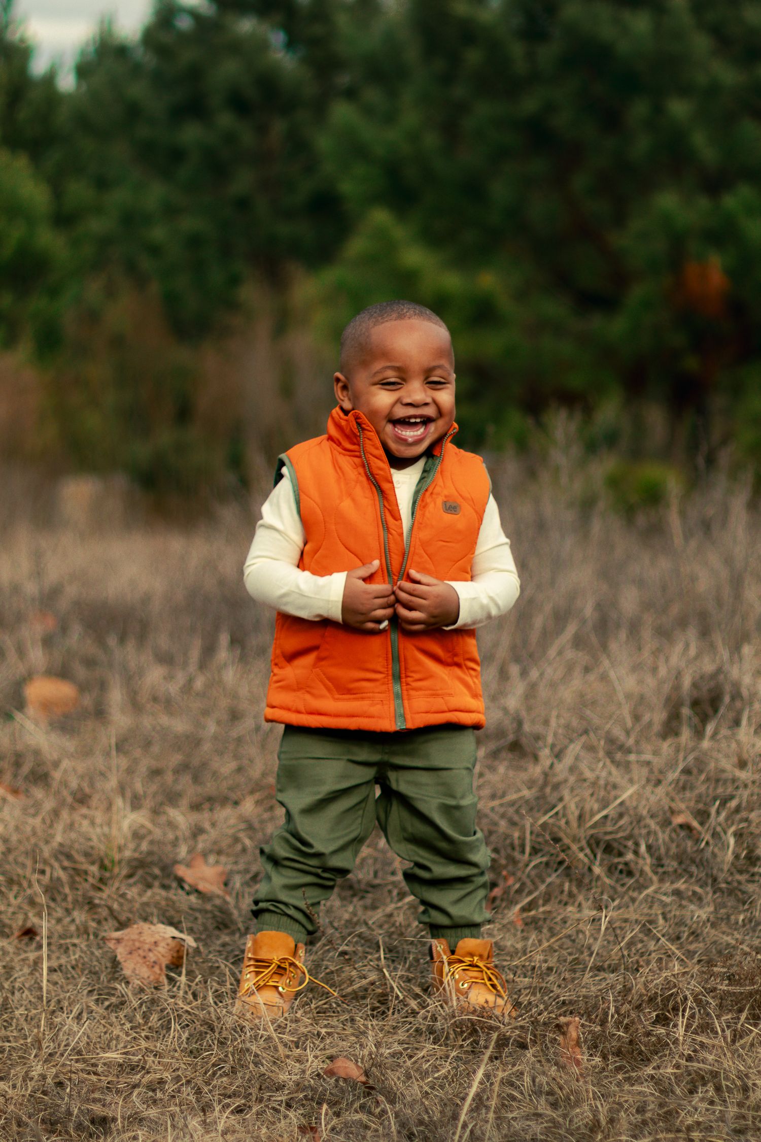 A series of four photos showing a child in an orange vest and brown boots laughing joyfully in a grassy field.