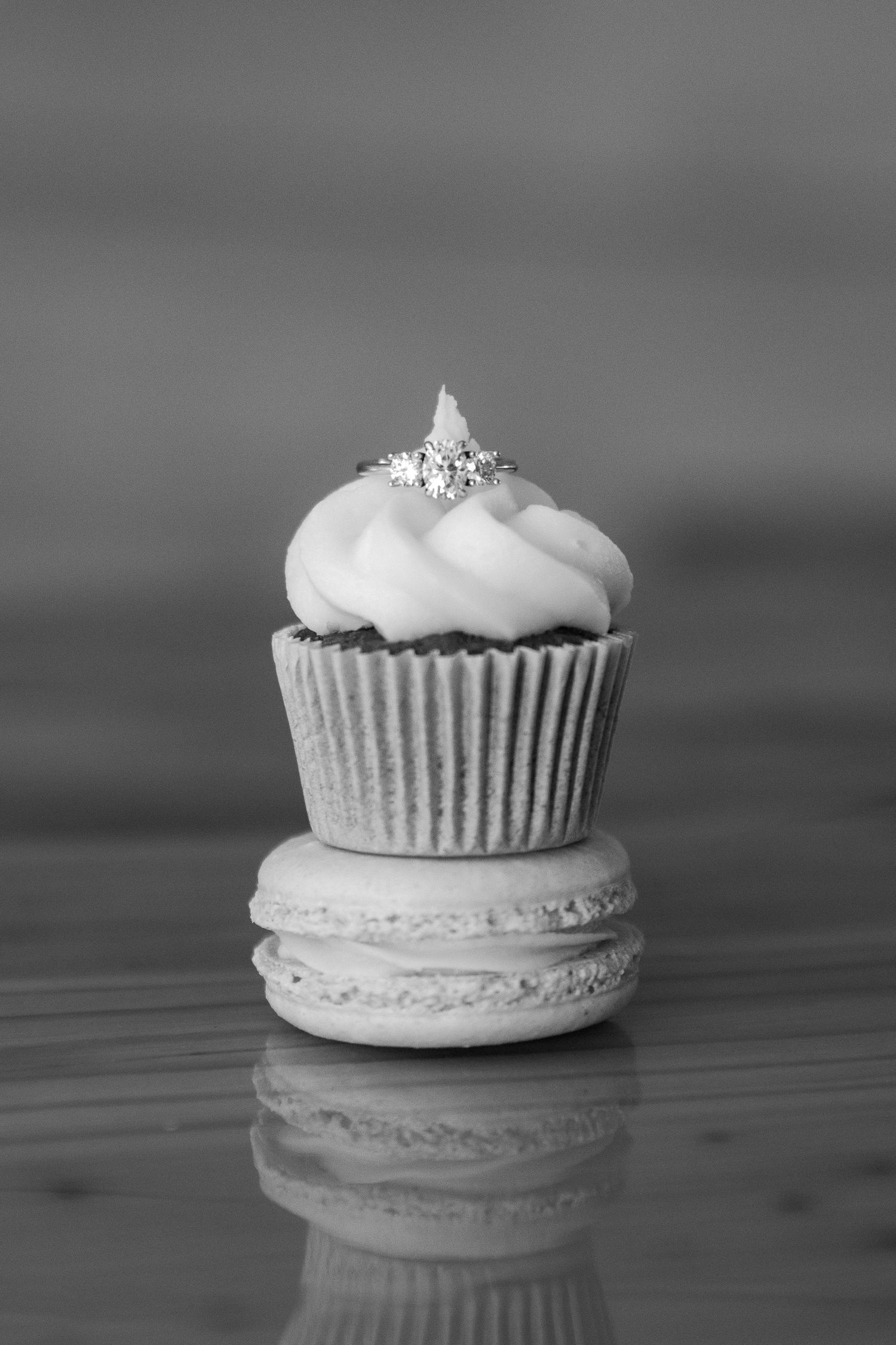 A black and white sequence of four images showing a cupcake being stacked on top of a macaron in progressive steps.