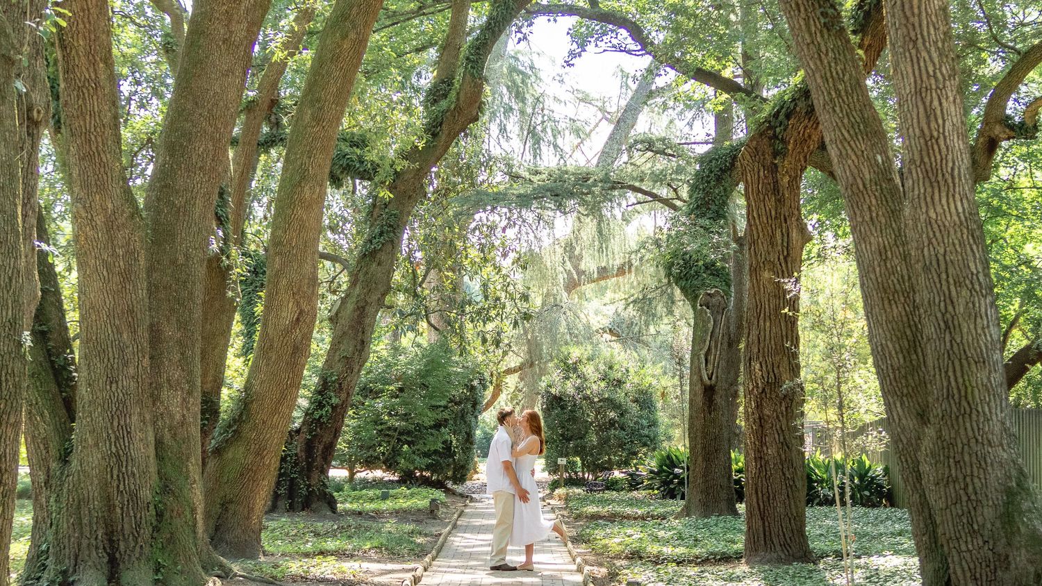 Engaged couple embracing beneath a canopy of oak trees on a garden path in Aiken, South Carolina.