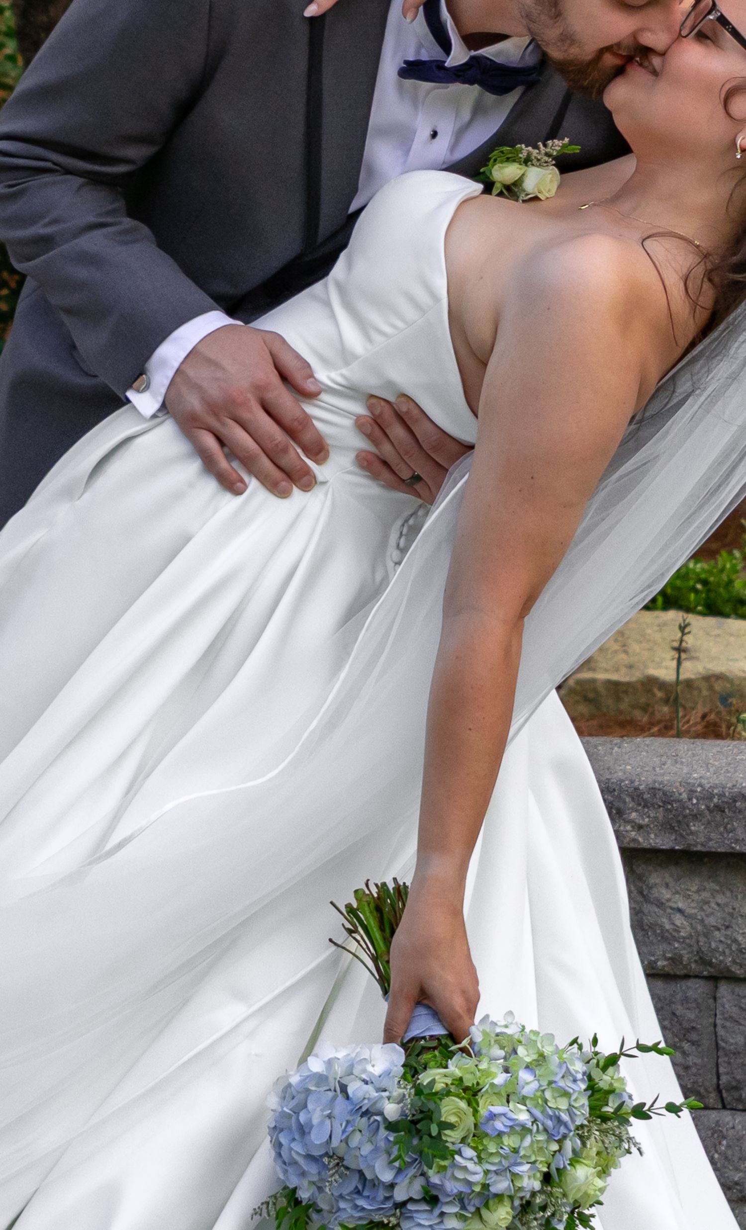 Bride and groom sharing a romantic kiss outdoors on their South Carolina wedding day, with the bride holding a blue hydrangea bouquet.