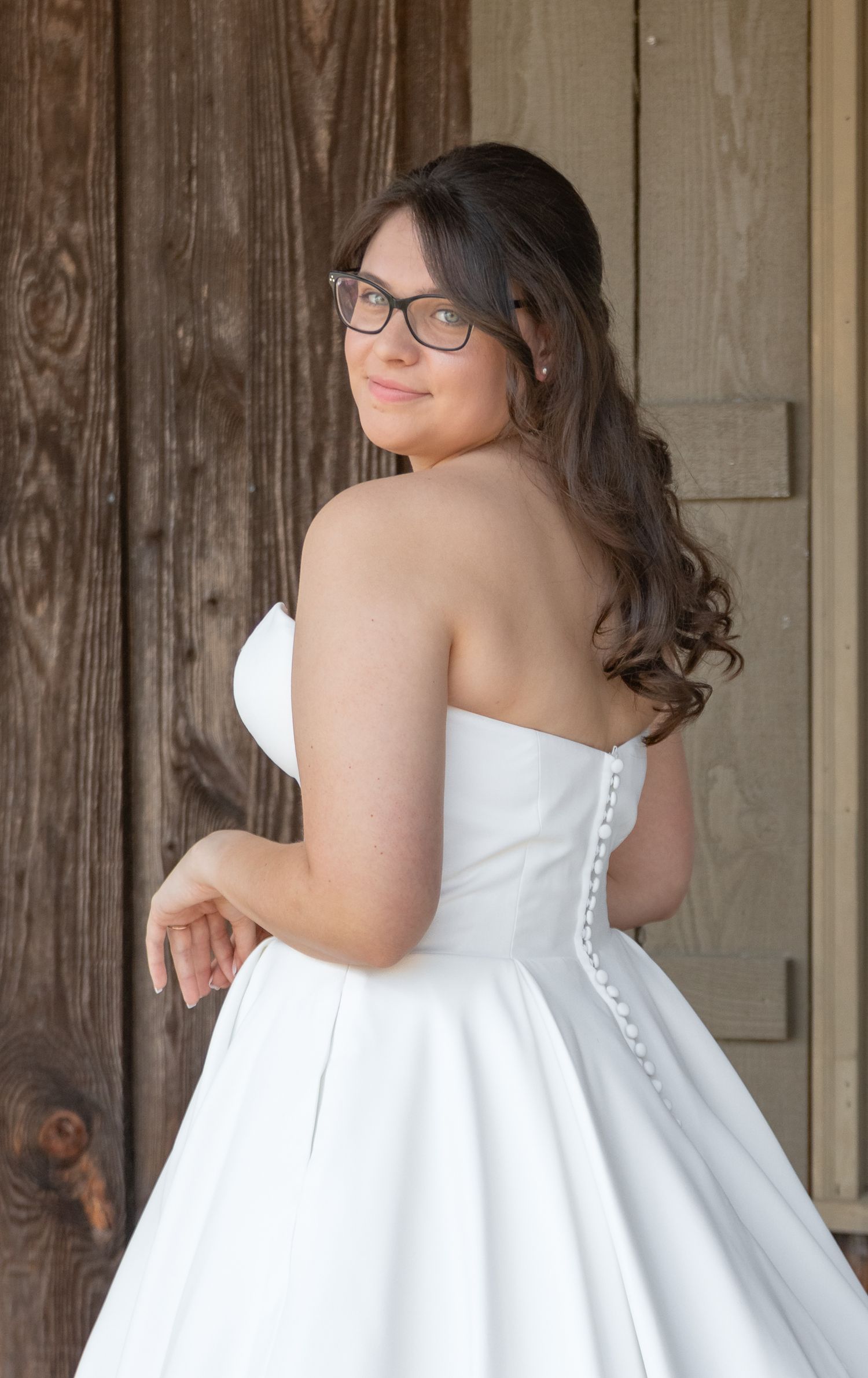 Bride in a strapless white wedding gown posing in front of rustic wooden doors during her South Carolina bridal portrait session.