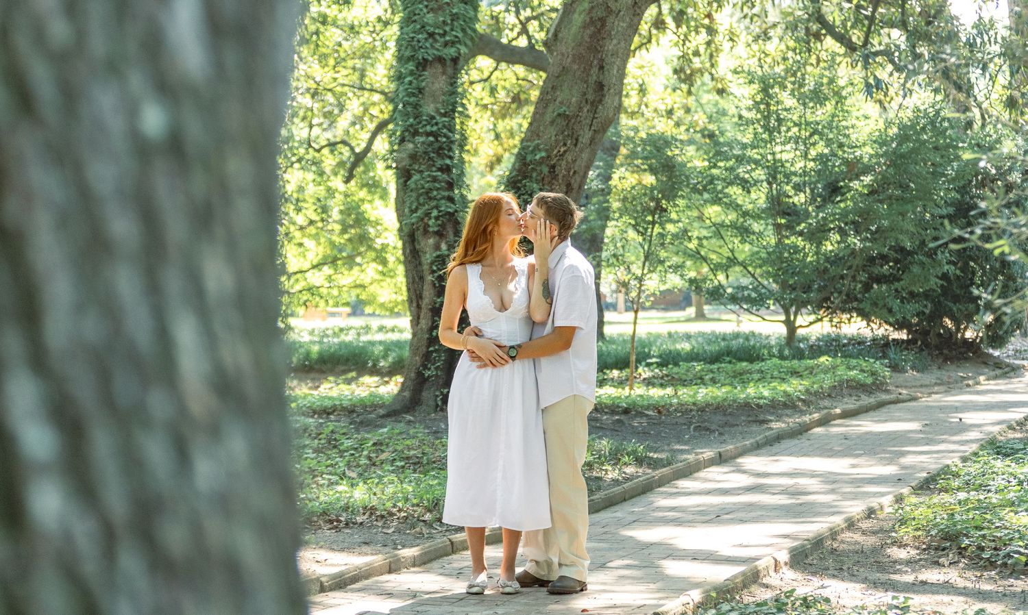 Engaged couple sharing a romantic kiss on a tree-lined garden path during an Aiken, South Carolina engagement session.
