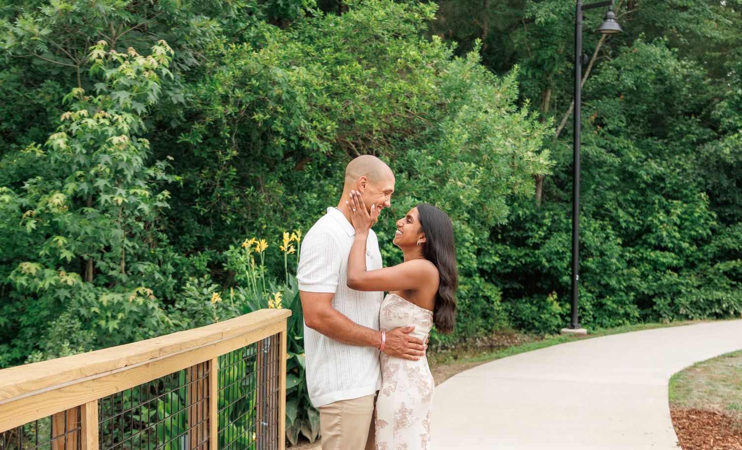 Couple sharing a tender moment on a scenic wooden bridge surrounded by lush green trees.