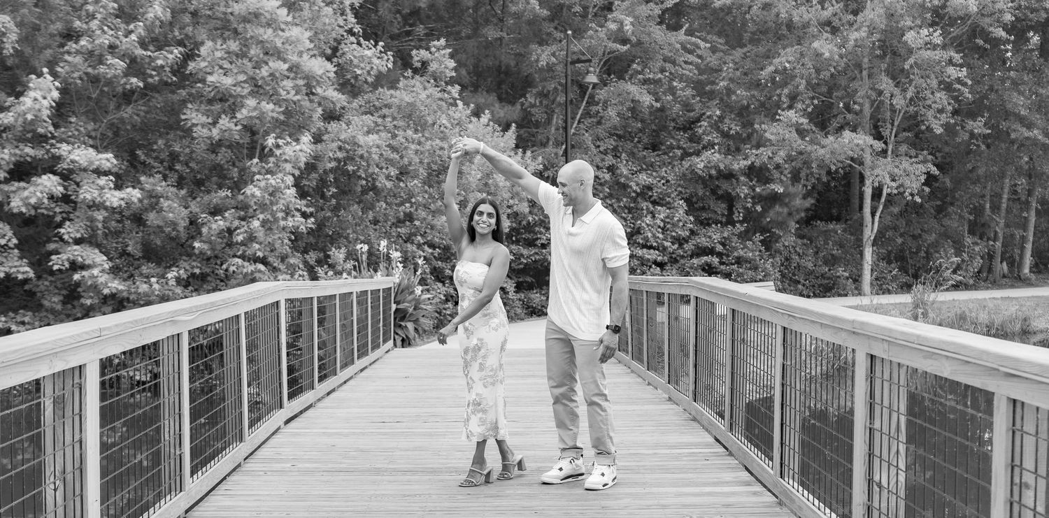 Black and white photo of couple dancing together on a wooden bridge outdoors.