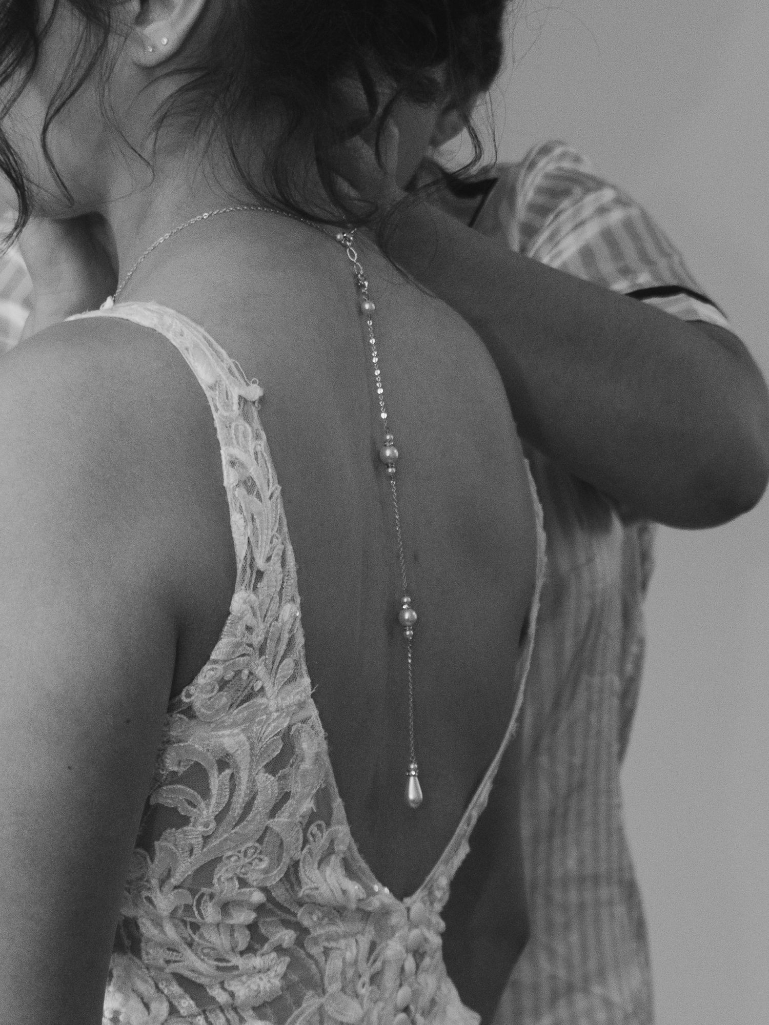 A black and white photograph shows a close-up view of an elegant lace-backed dress with delicate straps.