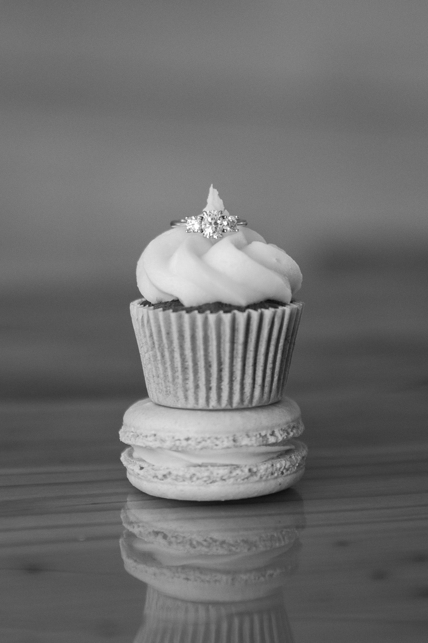 Black and white wedding dessert detail featuring a cupcake, macaron, and diamond ring topper.