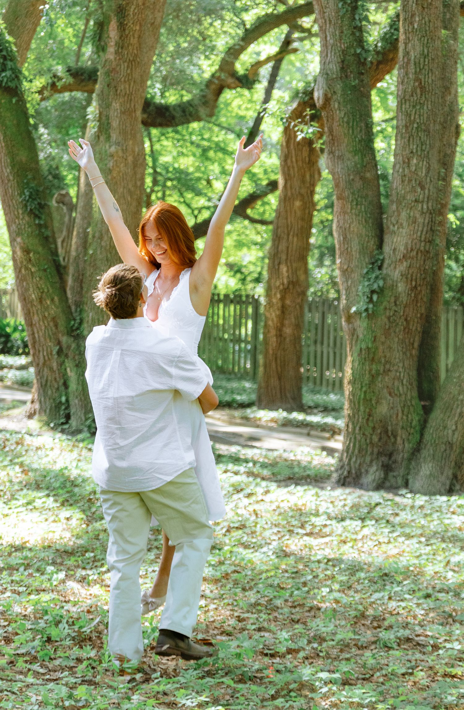 Engaged couple laughing as the groom lifts his partner among the trees during an Aiken, South Carolina engagement session.