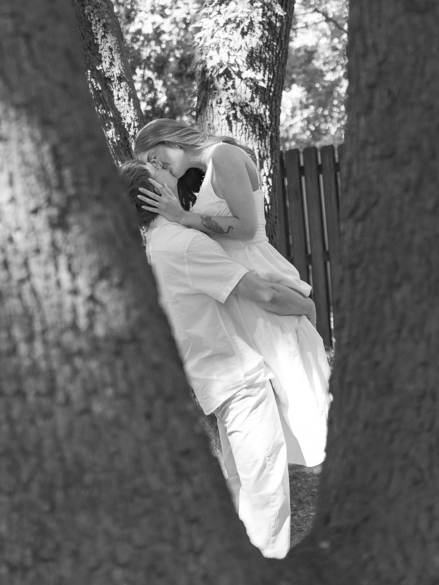 Black and white engagement portrait of a couple sharing a kiss between trees in Aiken, South Carolina.