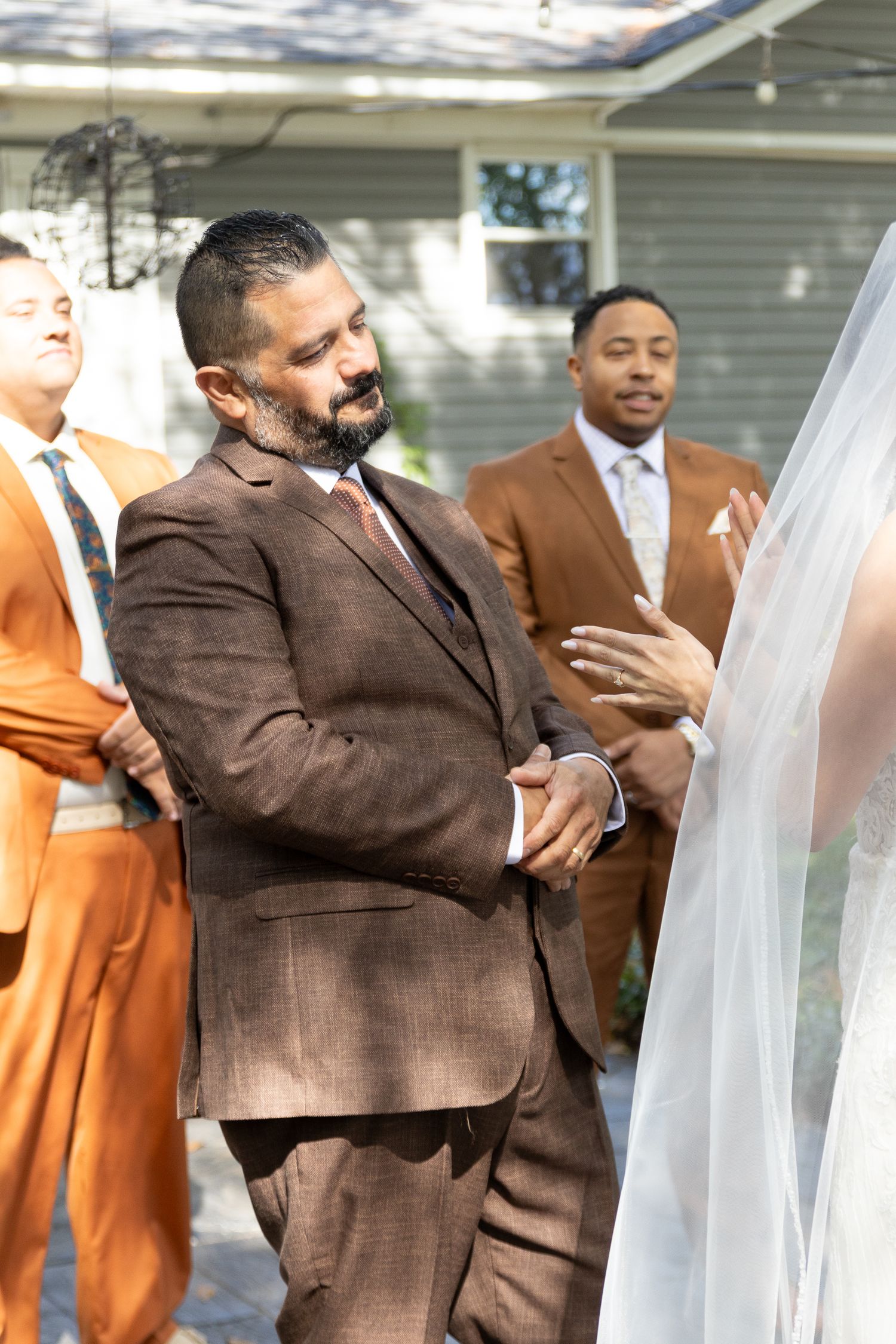 Wedding party members in brown suits and orange outfits line up during an outdoor celebration.