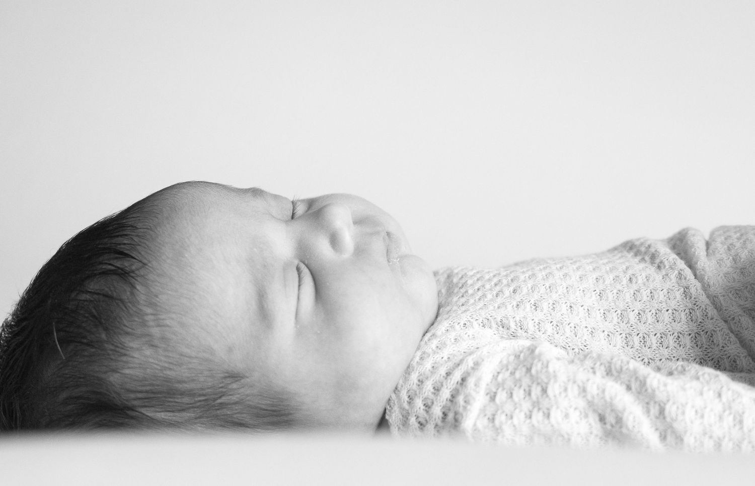 Peaceful sleeping newborn baby swaddled in white, captured in a soft black and white portrait photo.