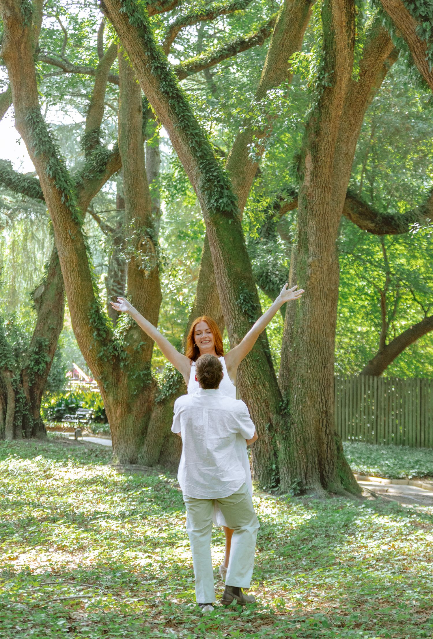 Engaged woman raising her arms joyfully among moss-covered trees during an Aiken, South Carolina engagement session.