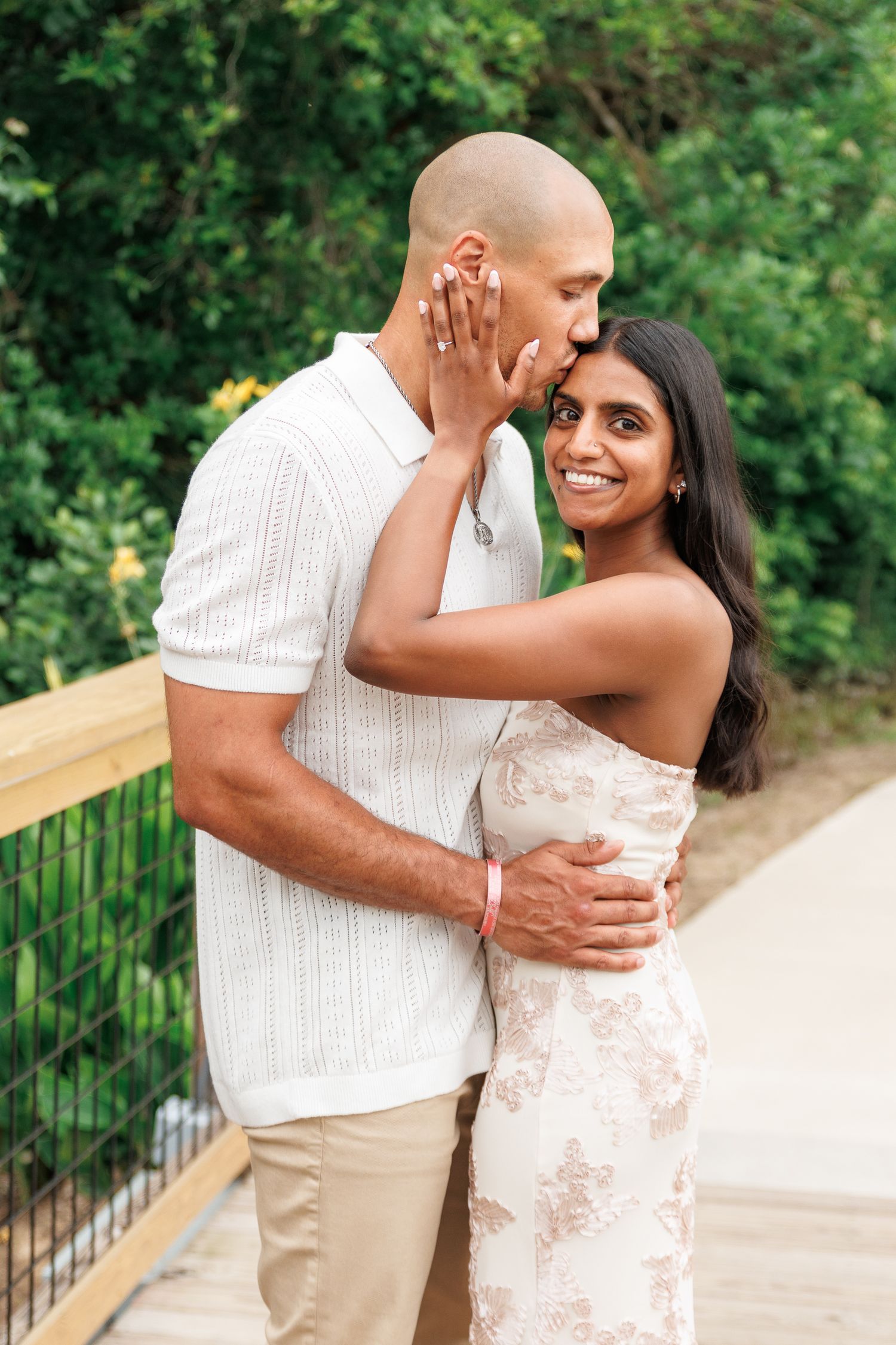 Happy woman smiling as her partner kisses her cheek on a wooden bridge.
