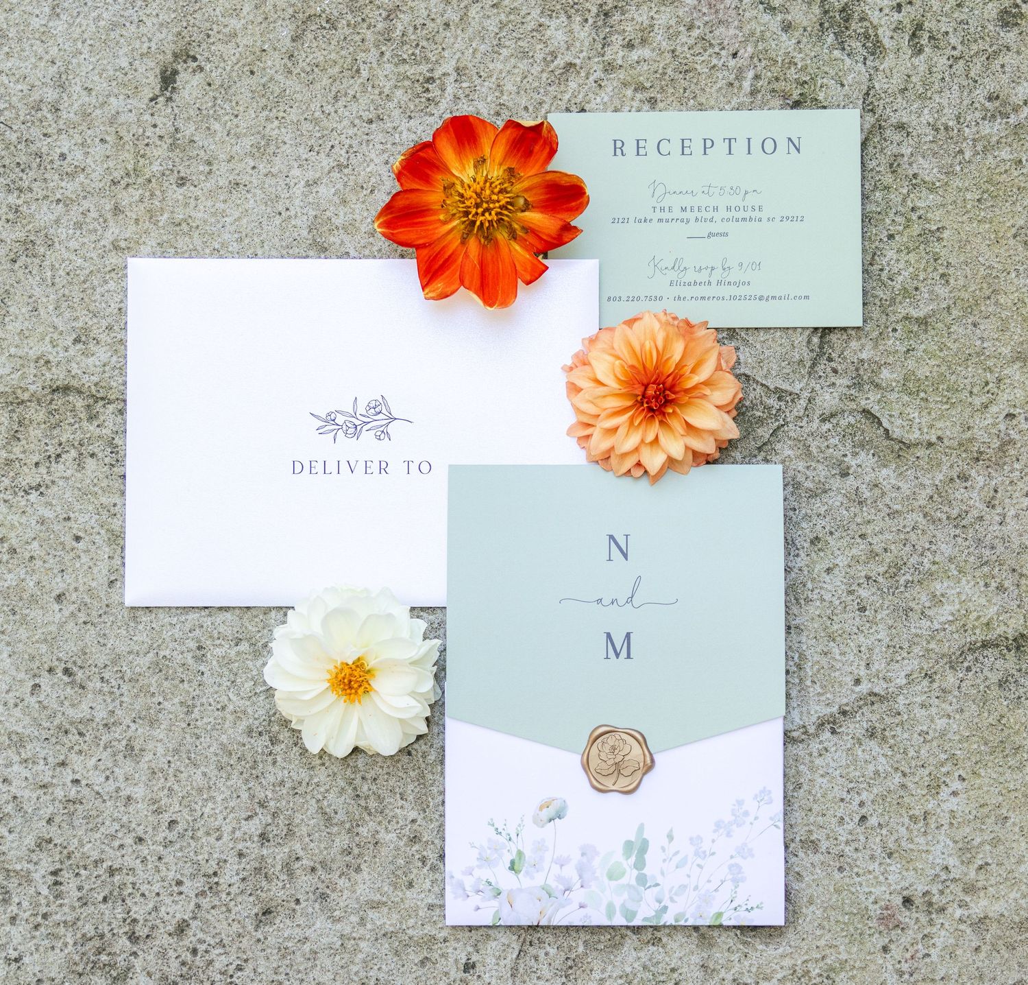 Wedding invitation suite with orange and white dahlia flowers arranged on concrete surface with reception and RSVP cards.