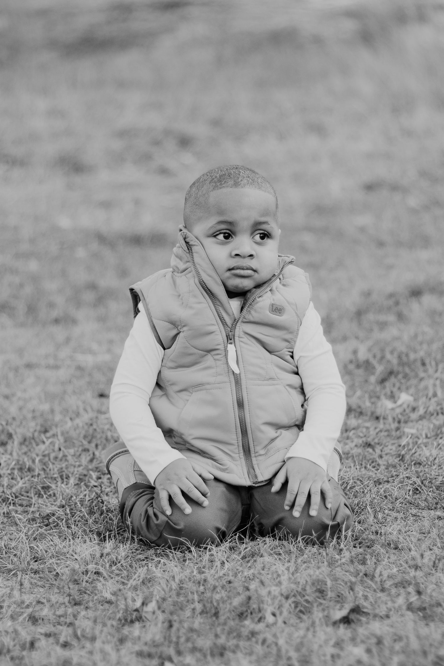 Black and white photo sequence showing a small child in a puffy vest sitting and crawling on grass.
