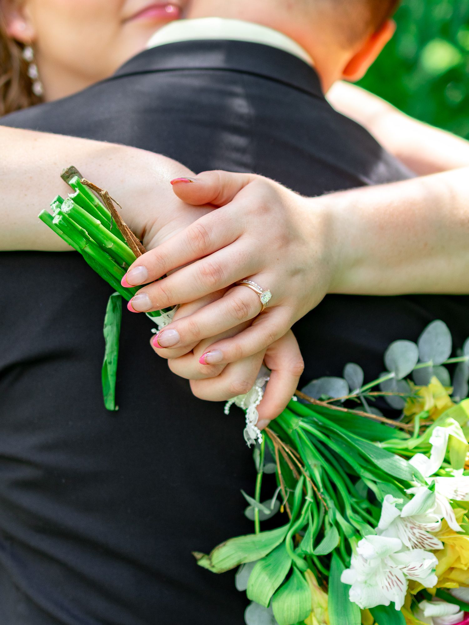 Bride embracing her groom while holding a white floral bouquet with a green ribbon on their wedding day.