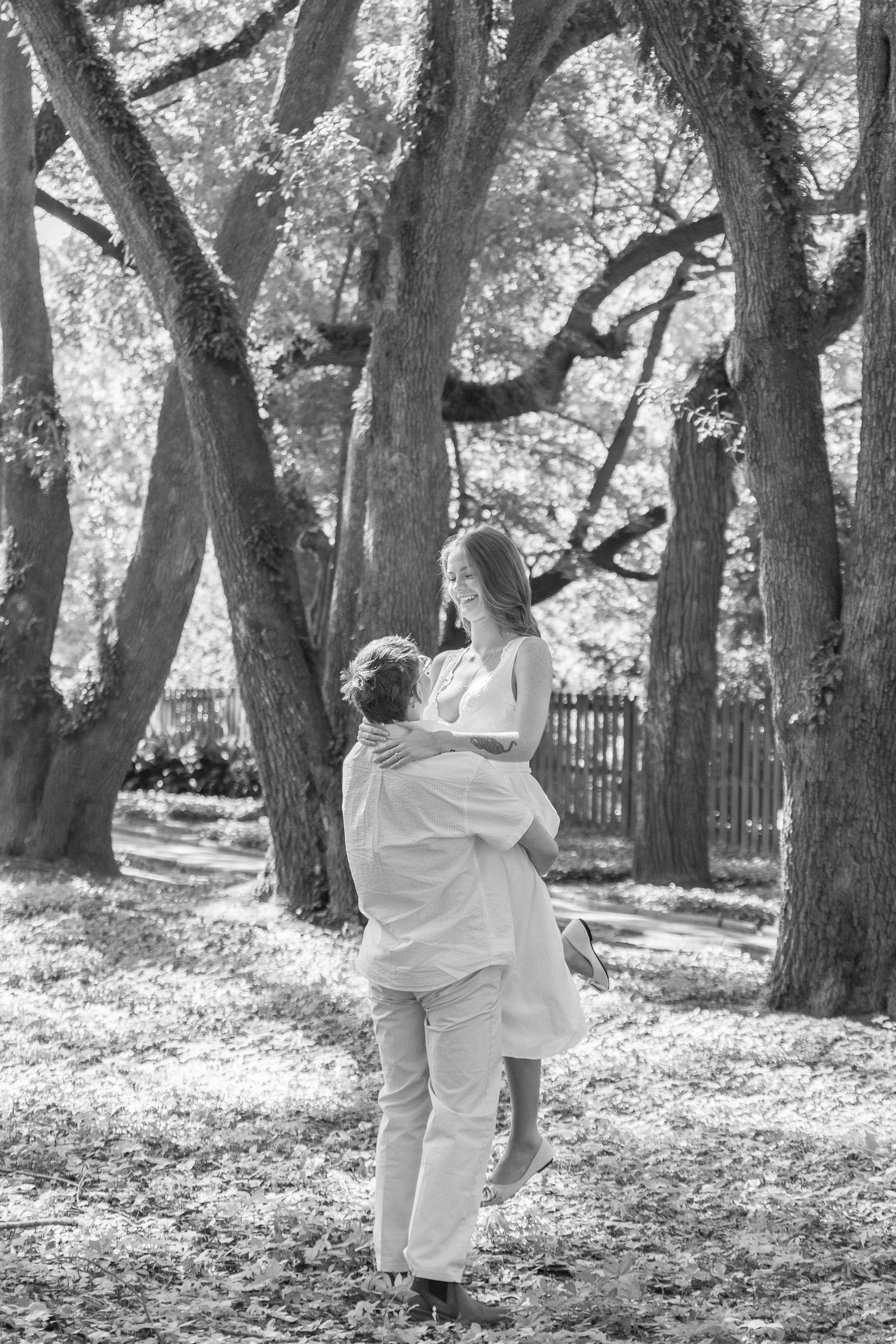 Black and white photograph of an engaged couple embracing beneath the trees in Aiken, South Carolina.