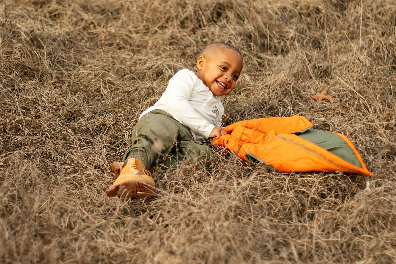 A person lying in dried grass wearing an orange jacket creates a playful series of rolling movements.