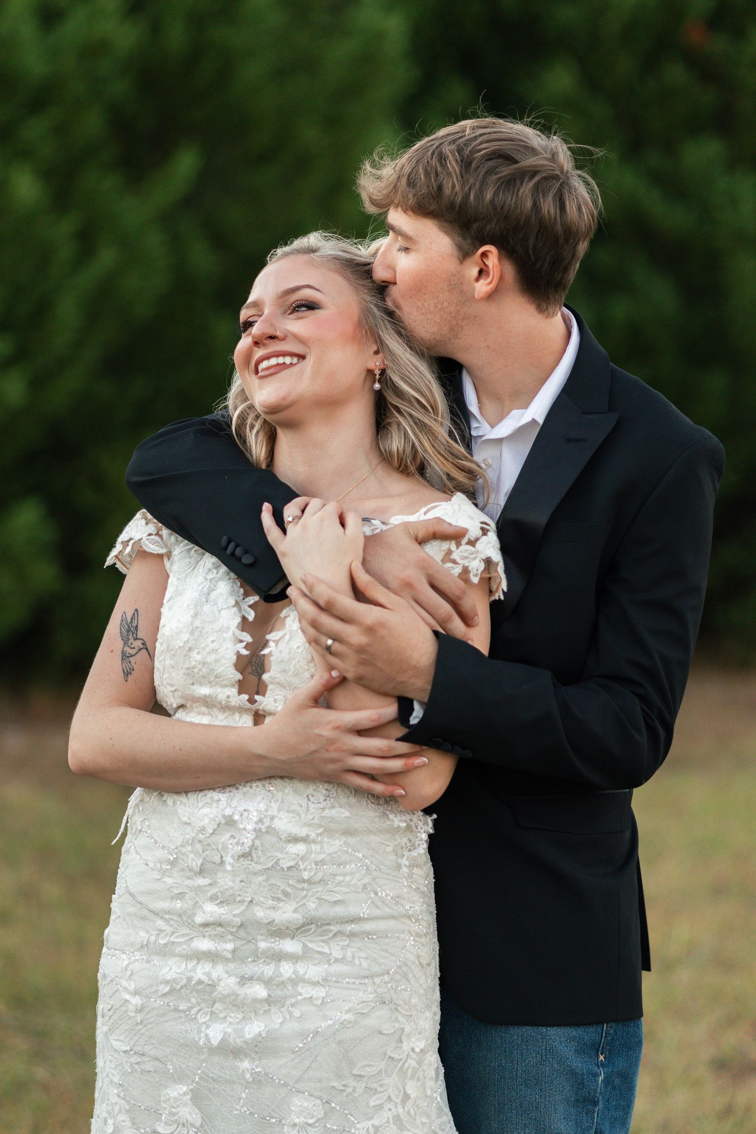A romantic outdoor wedding moment with a couple embracing, the bride wearing a lace dress and groom in a dark blazer.