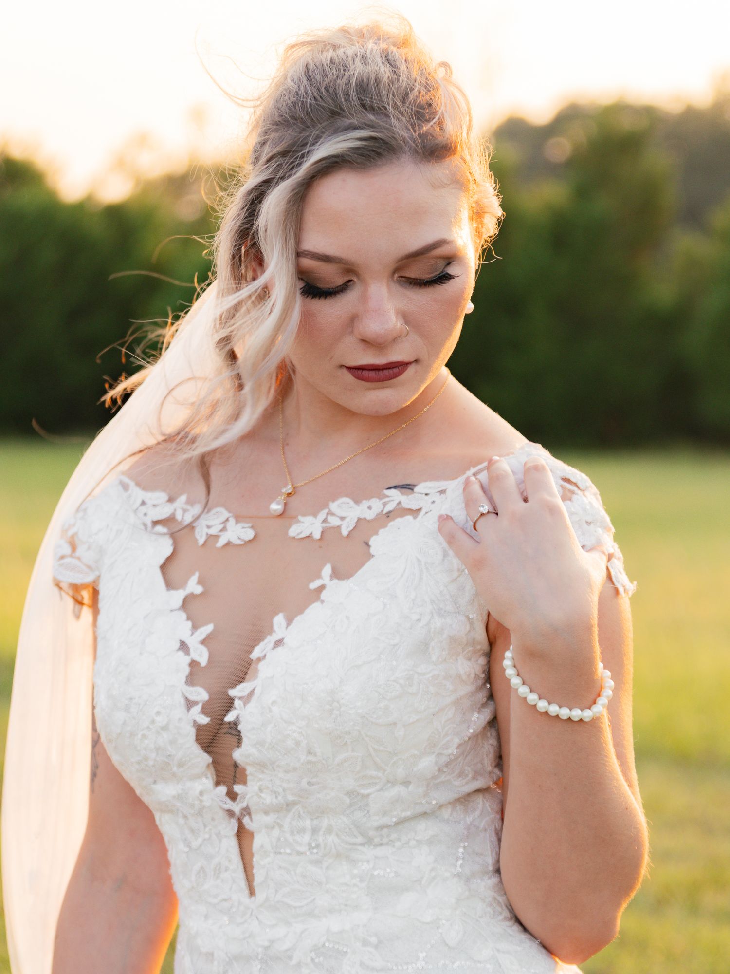 Close-up of bride in lace illusion neckline gown with pearl bracelet and necklace in sunset light.