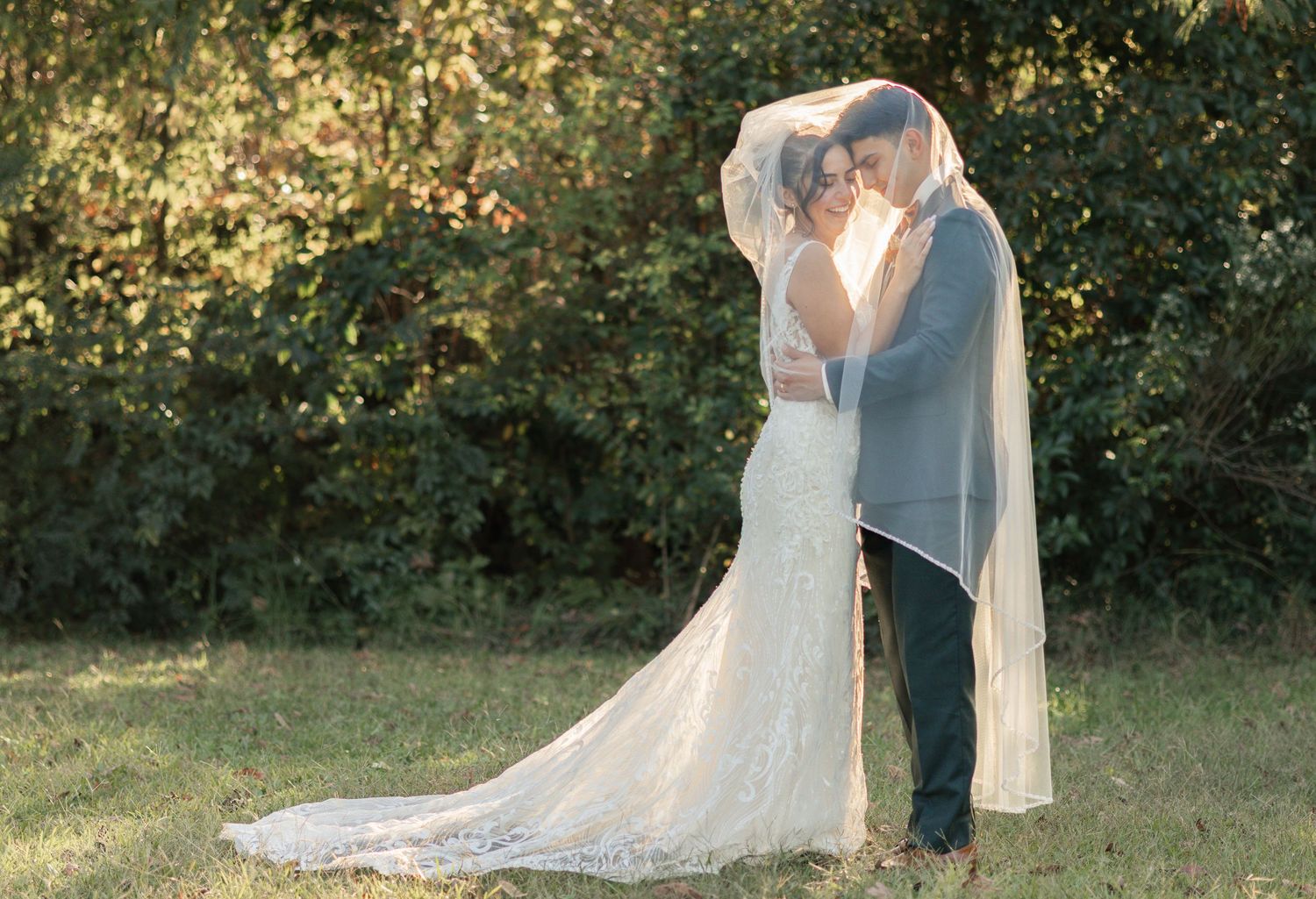 Couple sharing romantic kiss under bridal veil surrounded by lush autumn greenery.