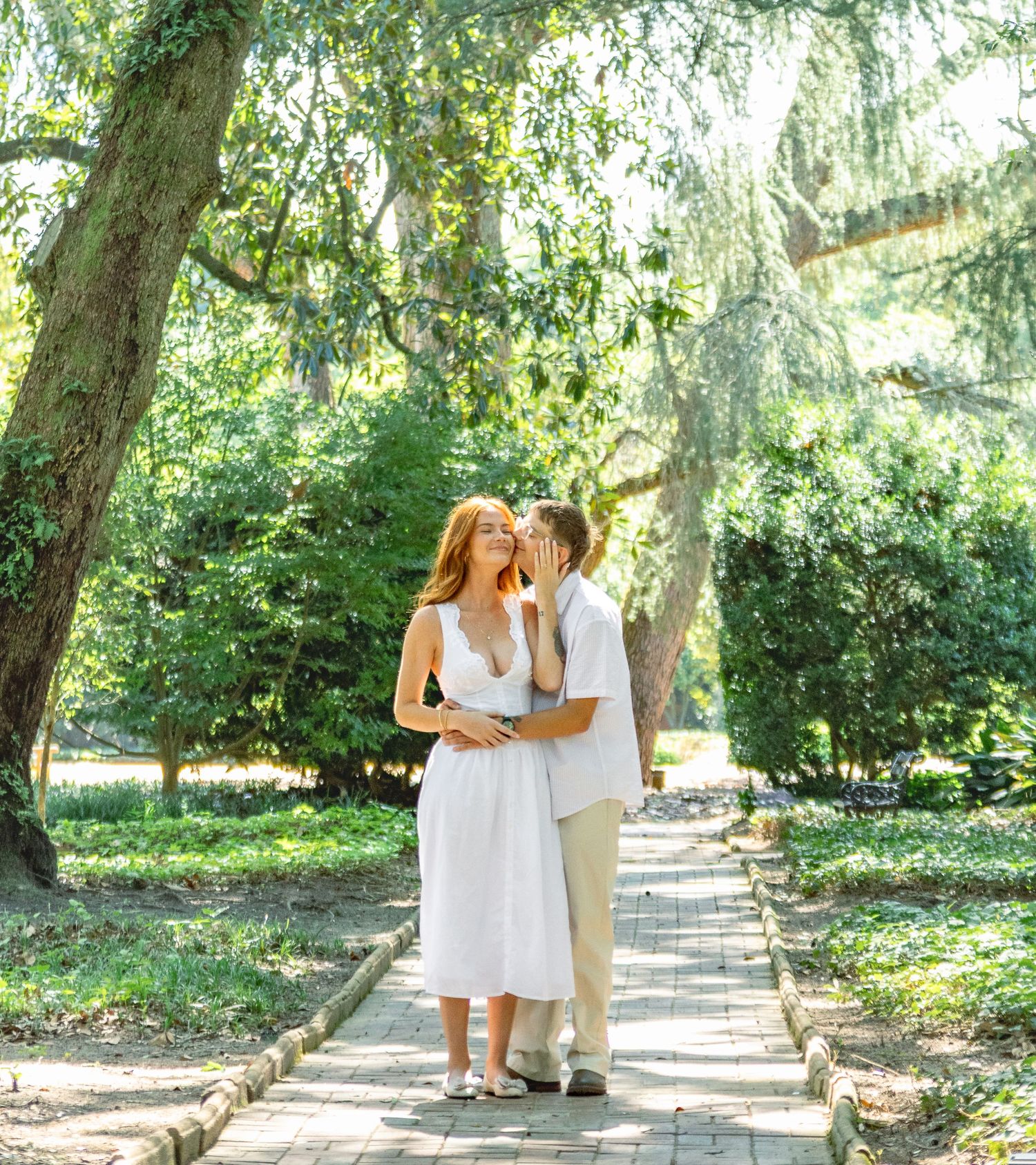 Engaged couple sharing a tender moment on a sunlit garden path during an Aiken, South Carolina engagement session.