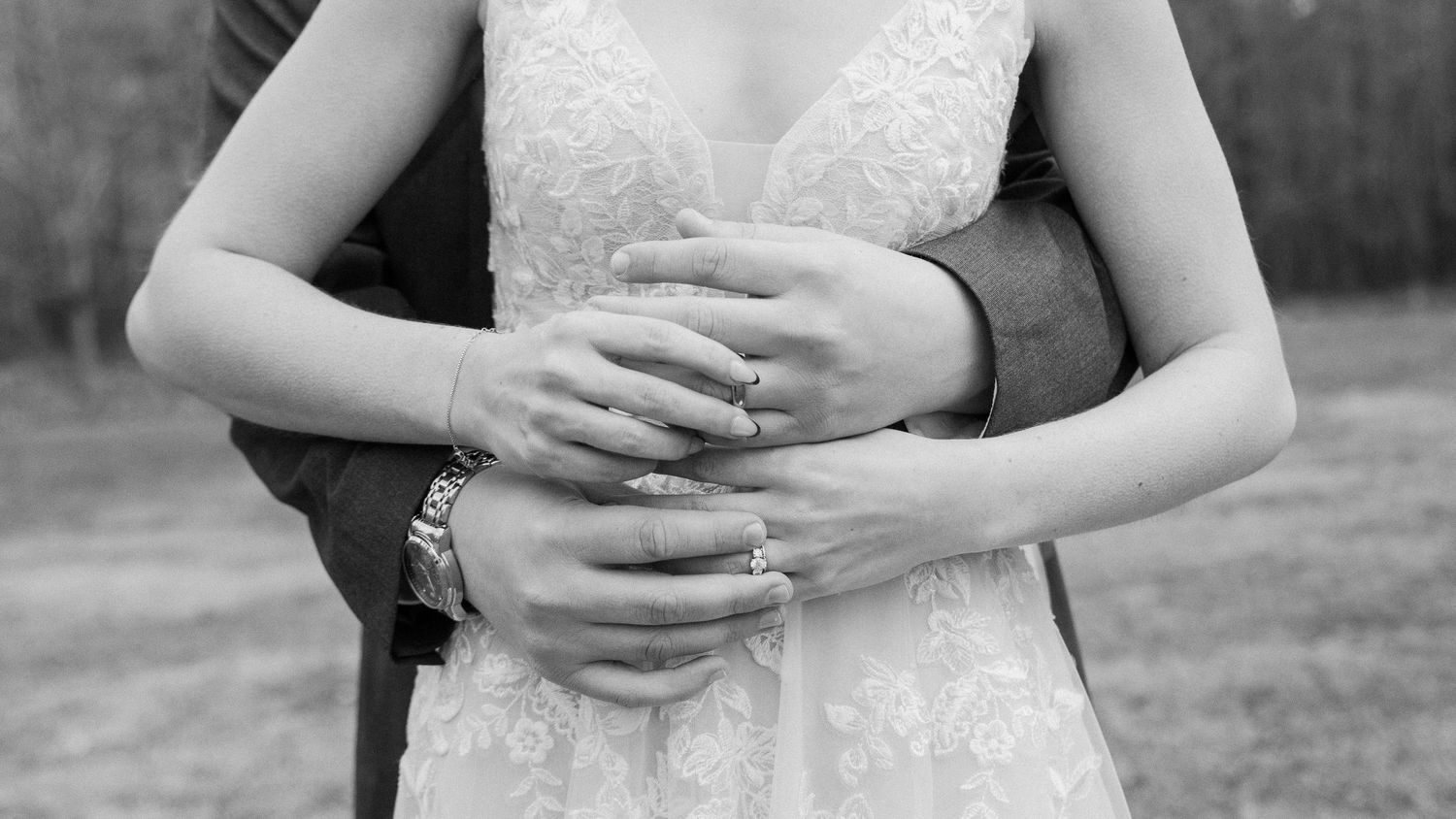A close-up black and white photo of hands clasped together in an intimate embrace.