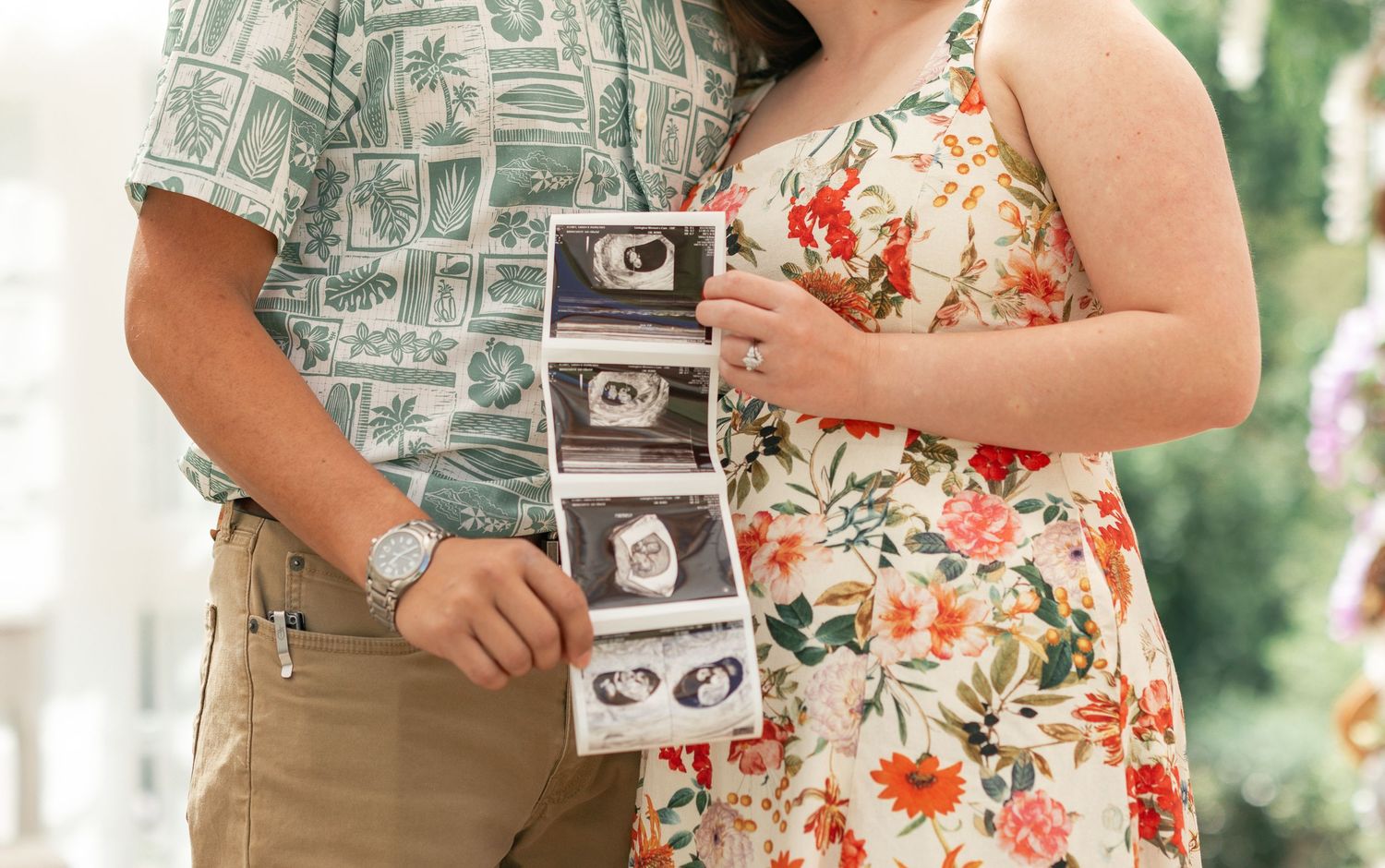 Couple holding ultrasound photos during pregnancy announcement in floral outfits.