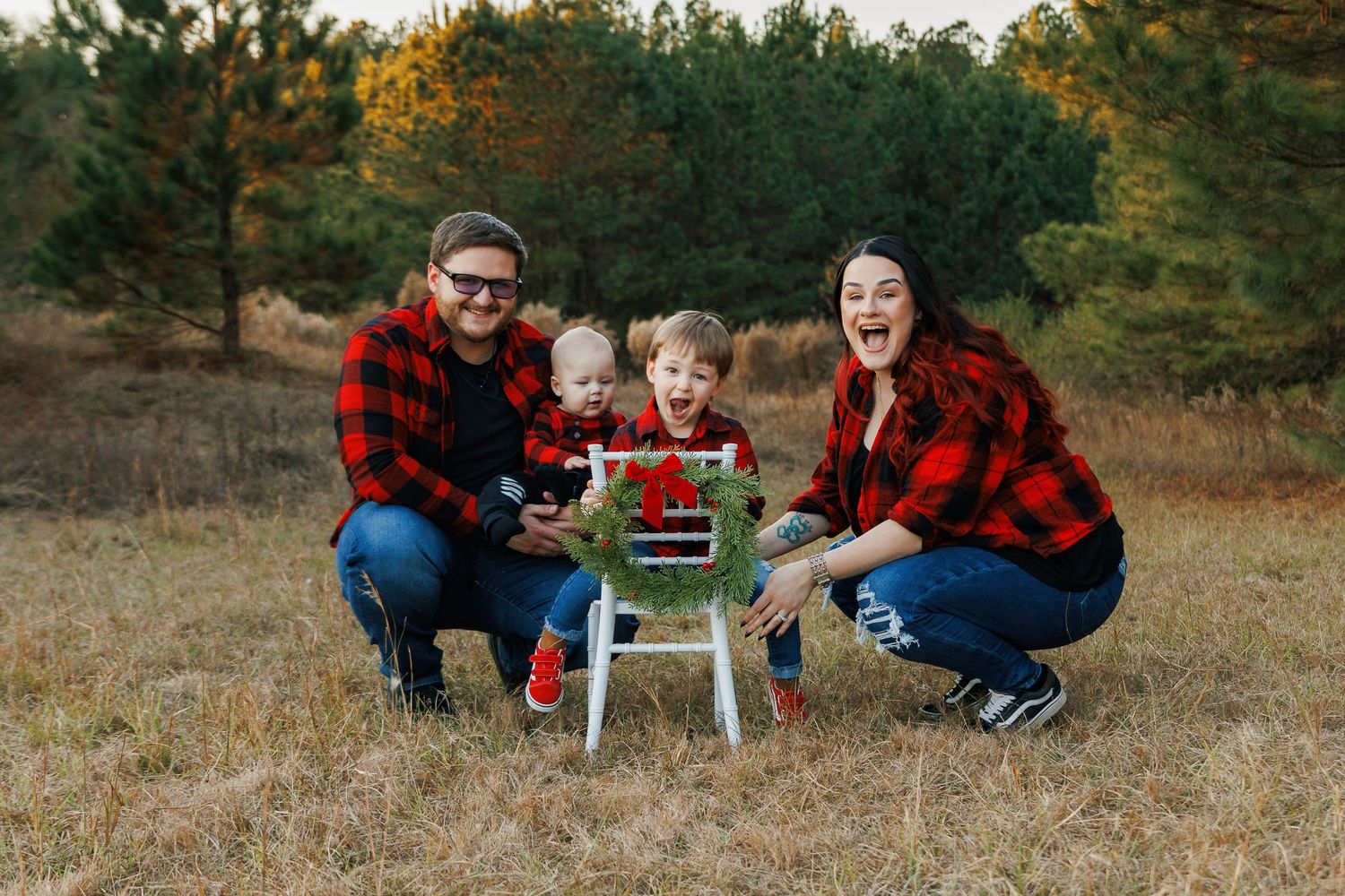 A family in red plaid poses with a festive holiday sled in a golden autumn meadow.